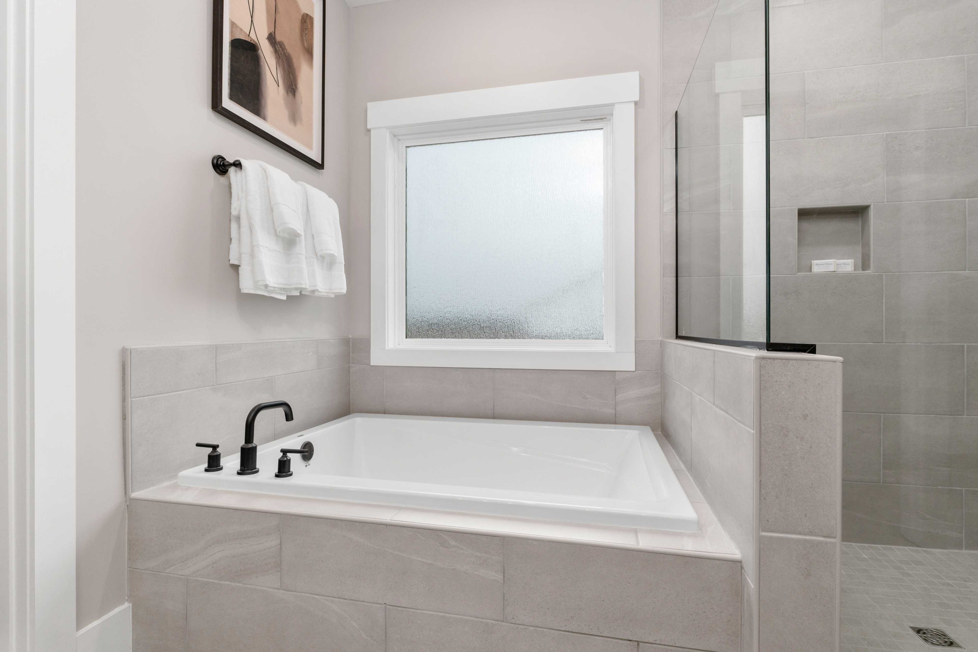 Spacious primary bathroom at Kendall Farms in Toney Alabama featuring soaking tub black faucet glass shower and frosted window