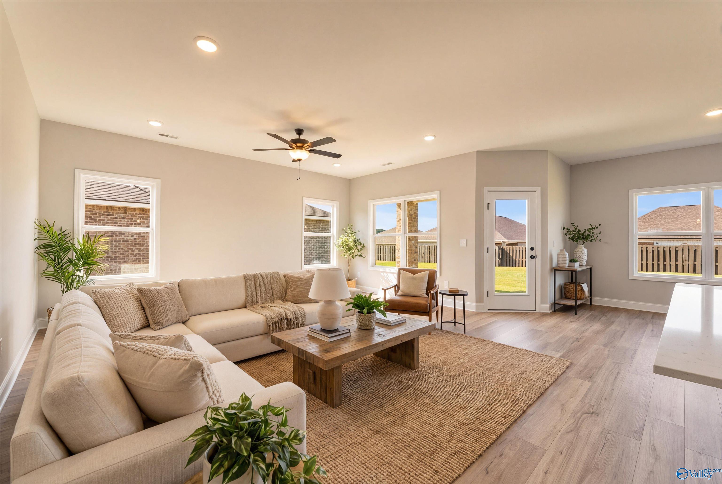 Spacious living room with beige L-shaped sofa, ceiling fan, plants, and backyard views in Davidson Homes Franklin B, Hazel Green, AL