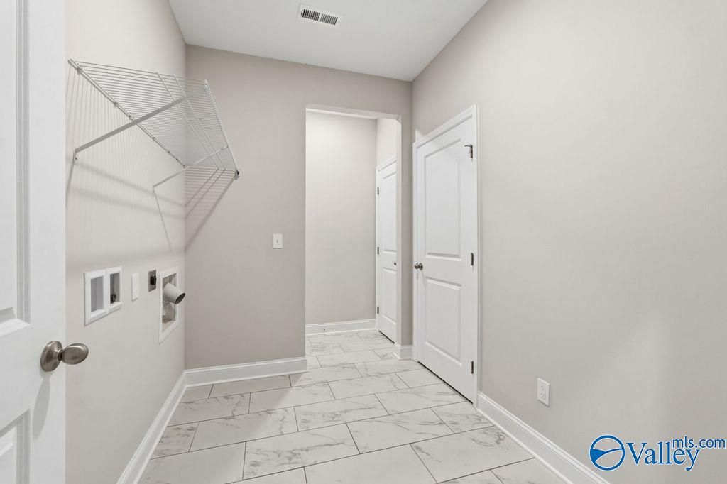 Modern laundry room featuring washer dryer hookups, wall rack, and marble tile floor in Davidson Homes The Harrison, Hartselle AL
