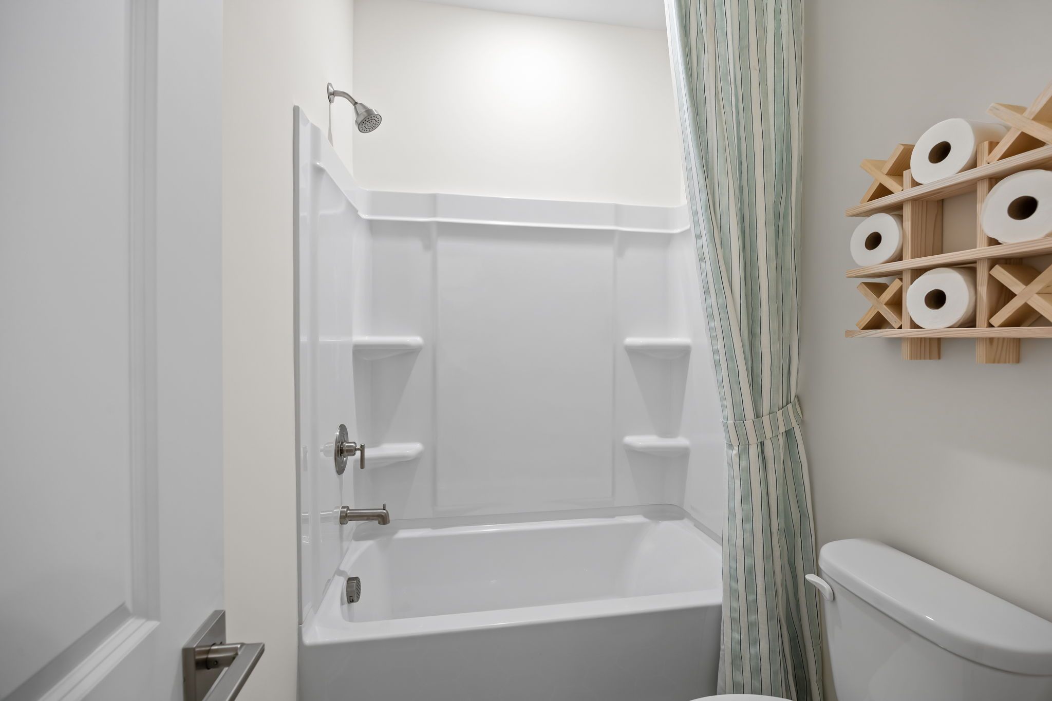 Modern bathroom with white tub-shower combo and decorative shelving at Springvale South in Fuquay-Varina, NC by Davidson Homes.