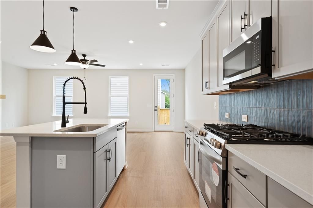 Modern kitchen with central island, gooseneck faucet, stainless appliances, blue tile backsplash in Davidson Homes The Marion A, Kennesaw, GA