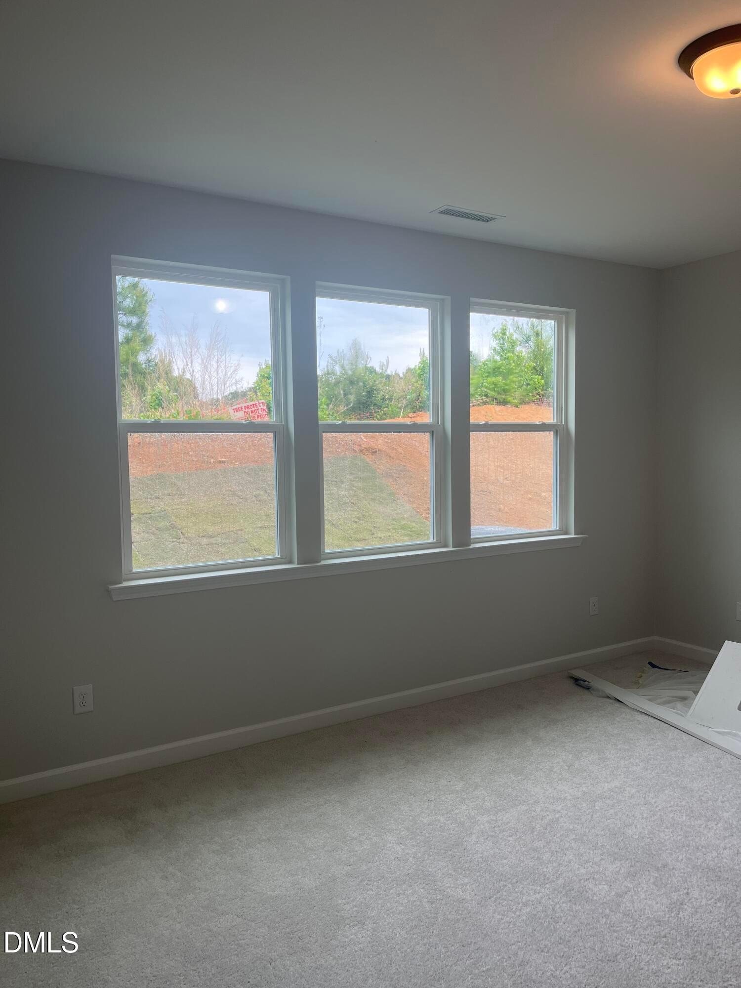 Bright empty bedroom with triple windows overlooking trees and lawn in Davidson Homes The Birch II E, Wake Forest, NC