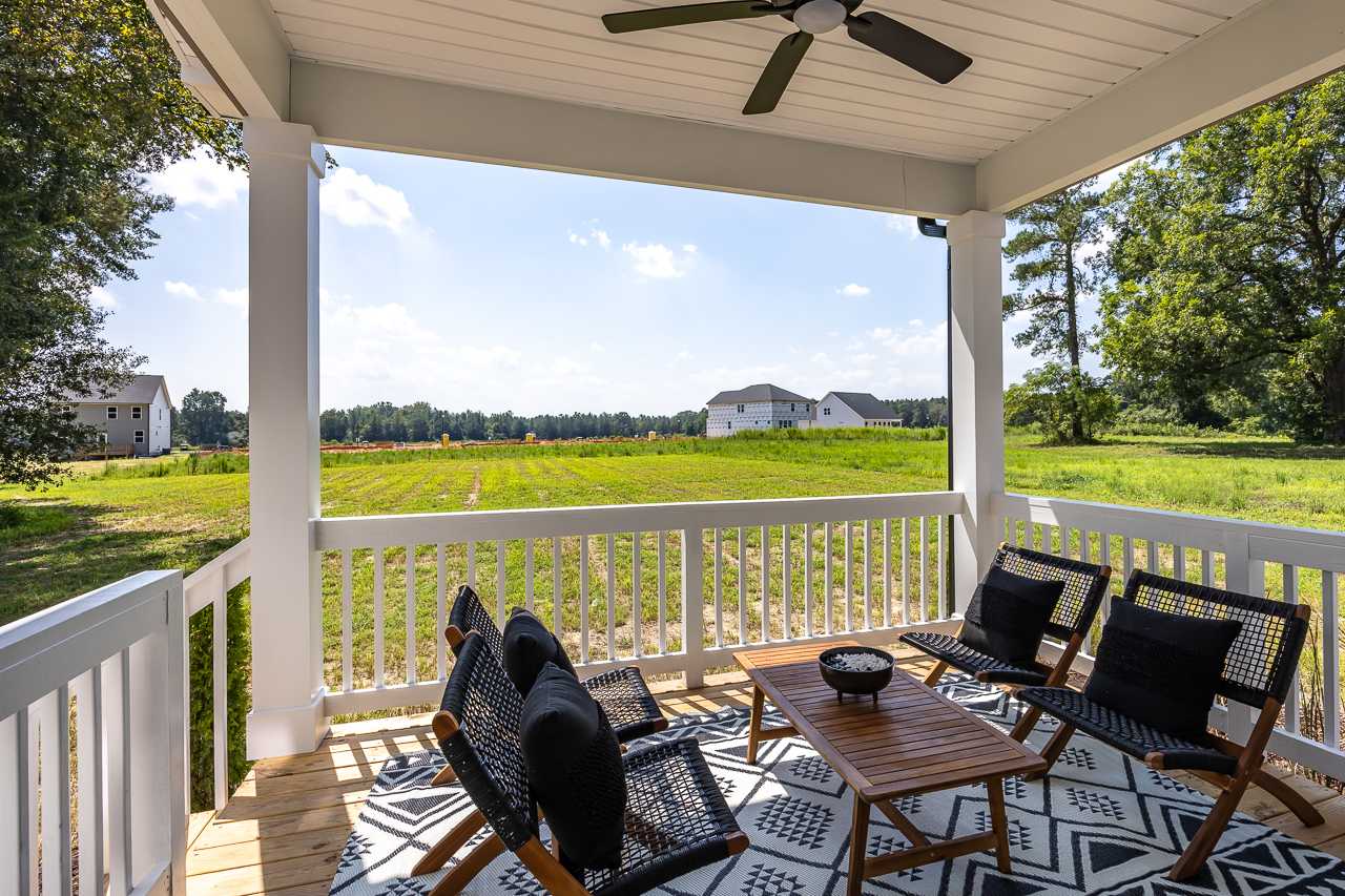 Covered deck with ceiling fan and outdoor seating overlooking green fields and farmhouse homes at Wellers Knoll in Lillington NC