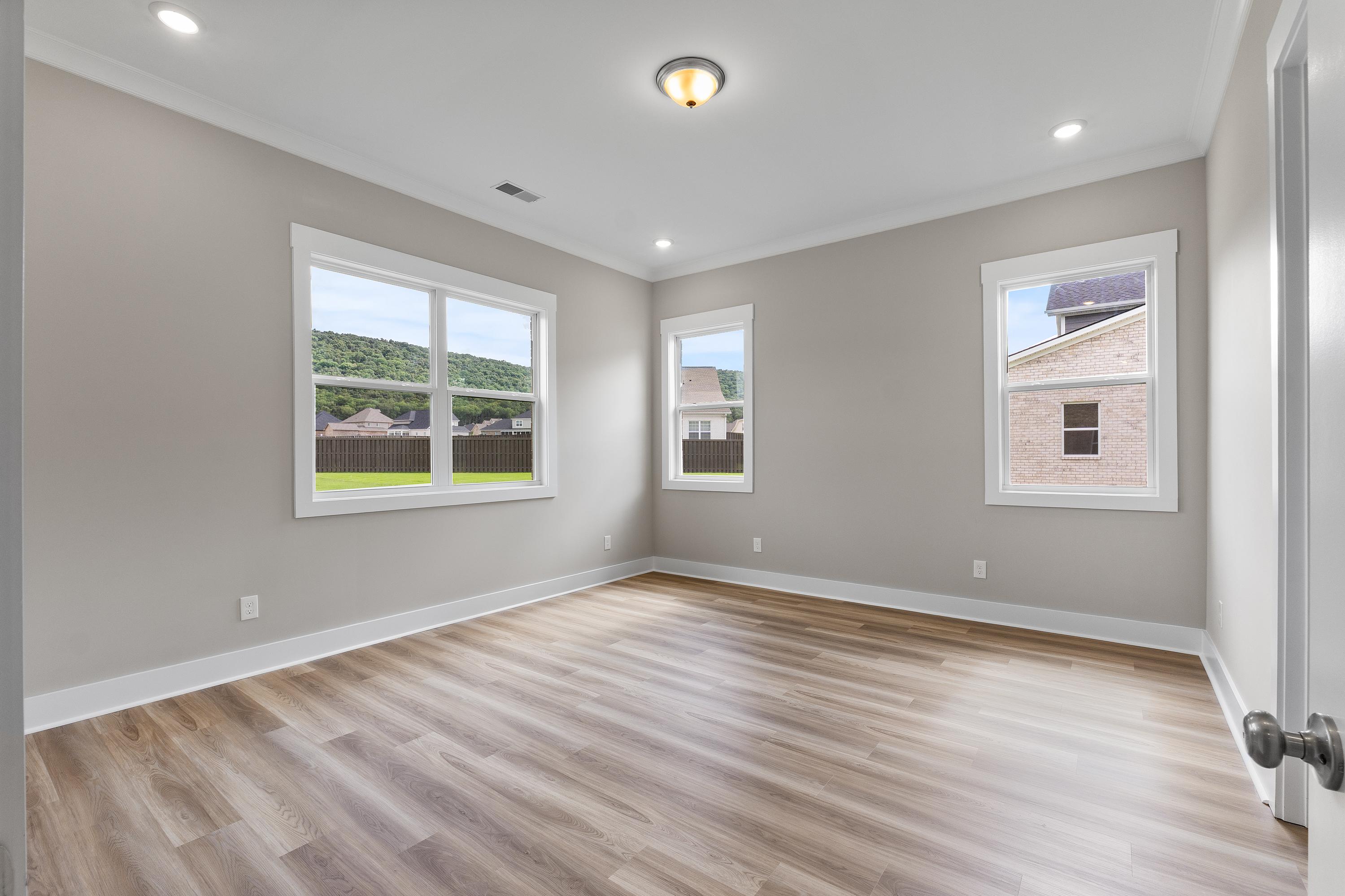 Spacious secondary bedroom in The Oxford C with neutral gray walls, large windows overlooking neighborhood, and luxury vinyl plank flooring