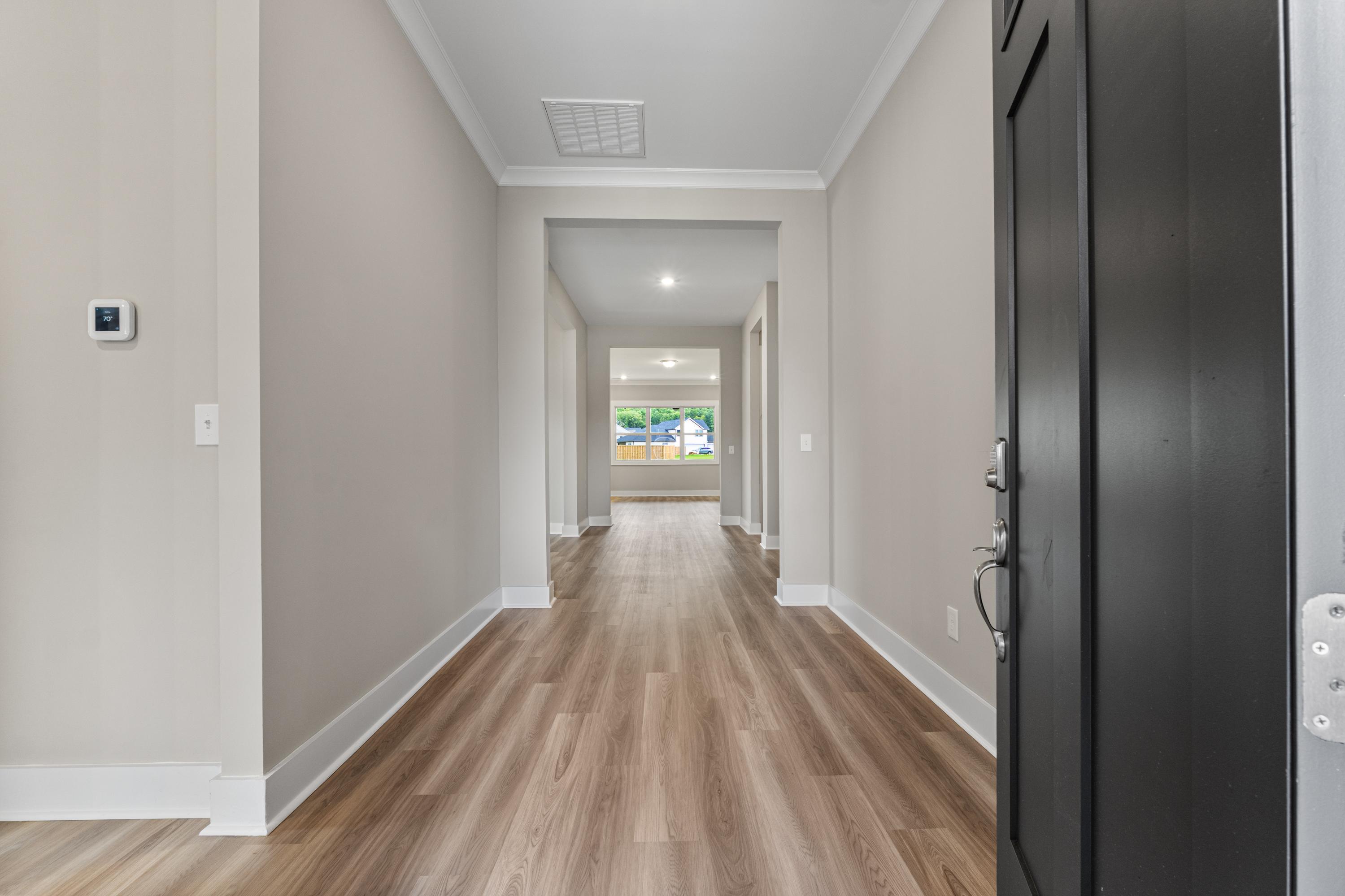 Spacious hallway in The Oxford C home with hardwood floors, neutral beige walls, black entry door, and sunlit window view