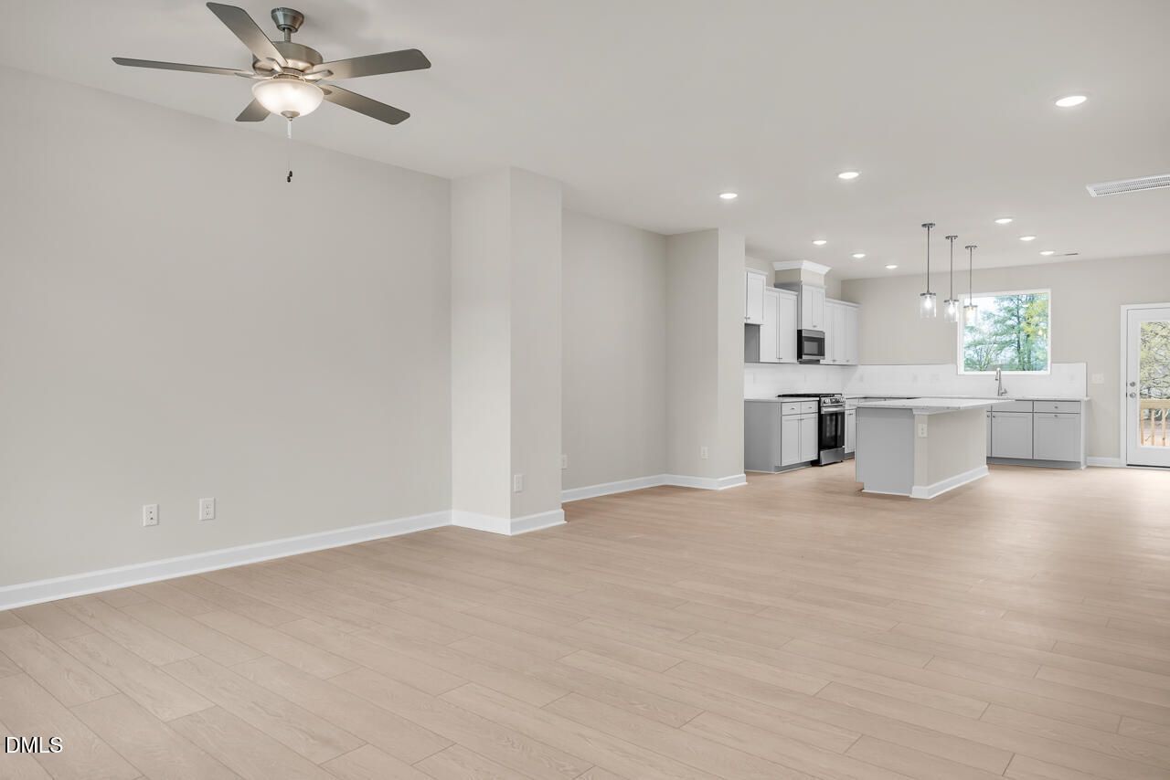 Open-concept kitchen with white cabinets, stainless appliances, island, and hardwood floors in Davidson Homes The Avery, Knightdale NC