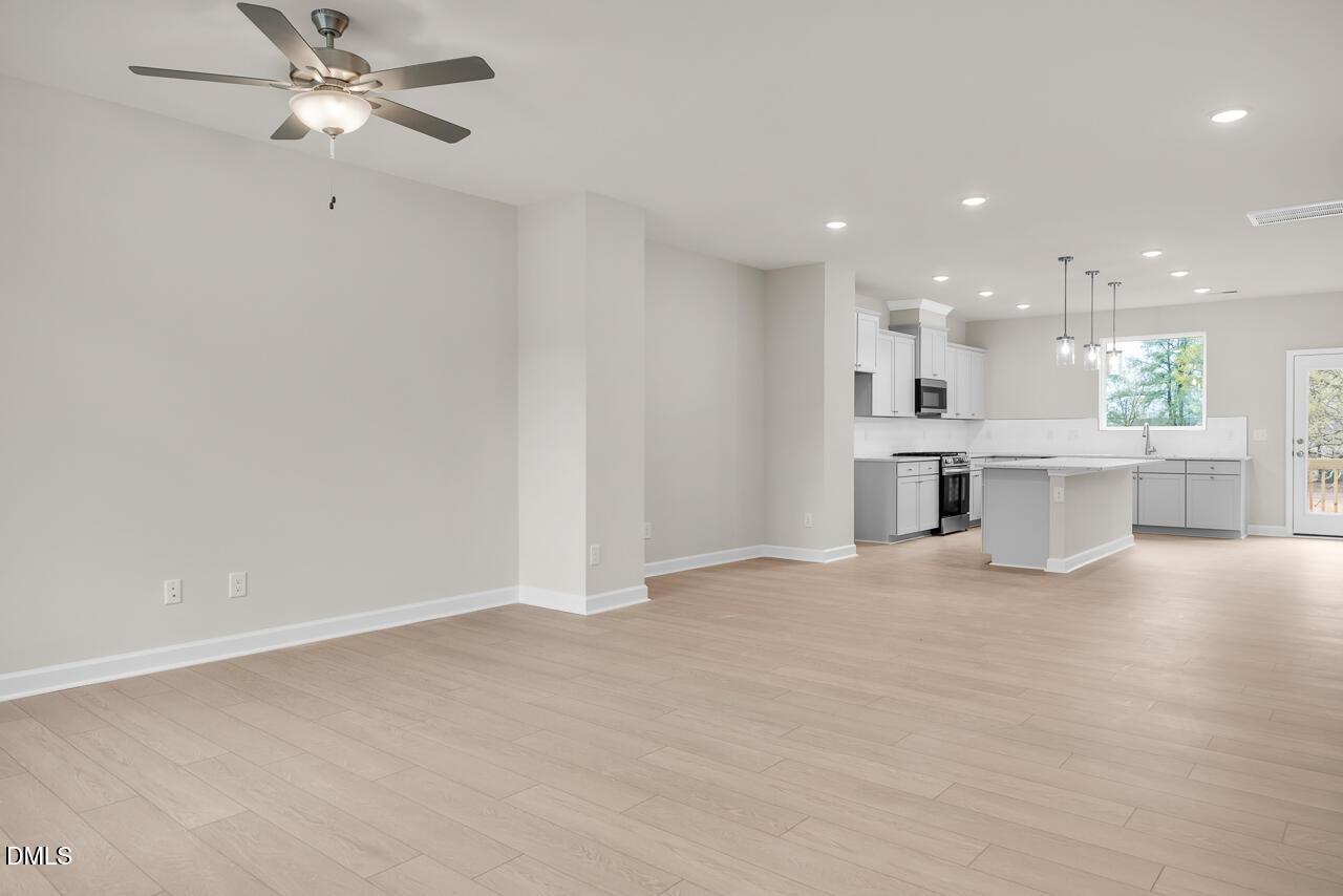 Open-concept kitchen with white cabinets, stainless appliances, island, and hardwood floors in Davidson Homes The Avery, Knightdale NC