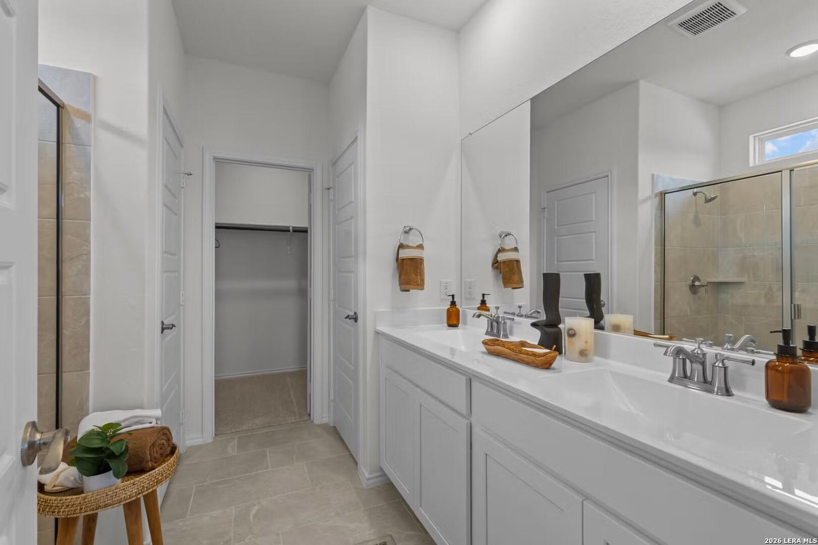 Modern master bathroom with white double vanity, glass shower, walk-in closet in Davidson Homes The Daphne K, San Antonio