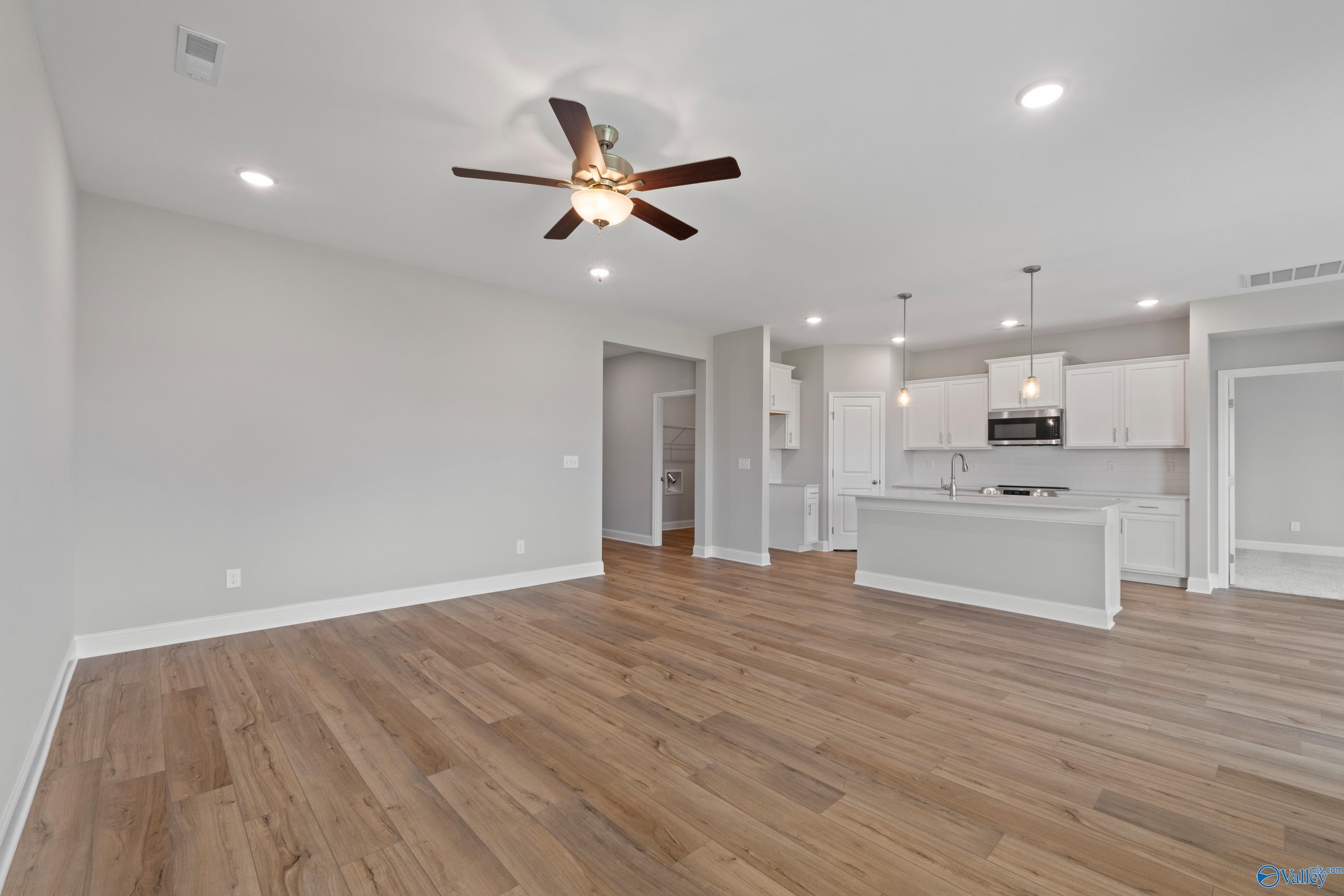 Open-concept living-kitchen with hardwood floors, white cabinets, island, and ceiling fan in Davidson Homes The Everett B, Toney, Alabama