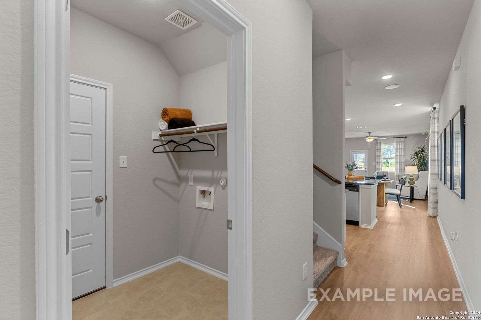 Modern laundry room with washer-dryer space, towel shelves, and hangers opening to hallway and kitchen in Davidson Homes The Sabine B, San Antonio