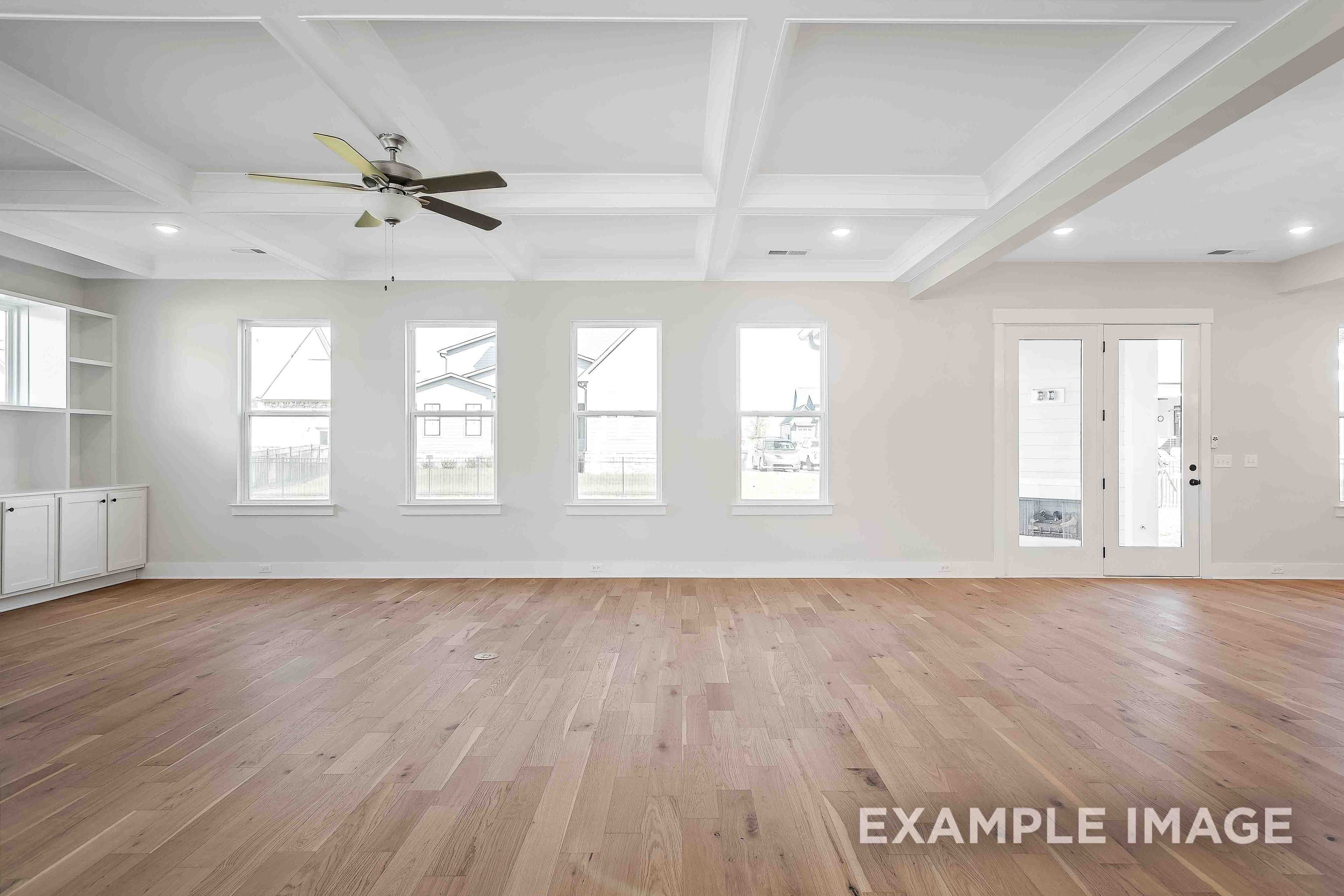 Spacious living area in The Alston A with light oak hardwood floors, tray ceiling fan, large windows, and French doors