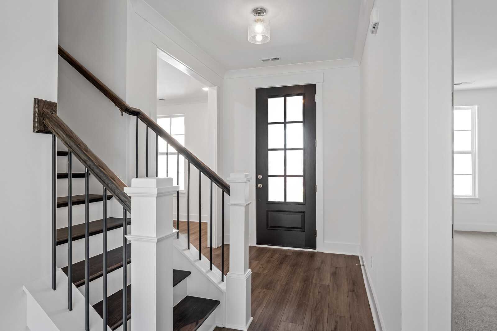 Elegant wooden staircase with black iron balusters and dark glass door in The Hawkins 2-story home, Shelton Square, Murfreesboro, Tennessee