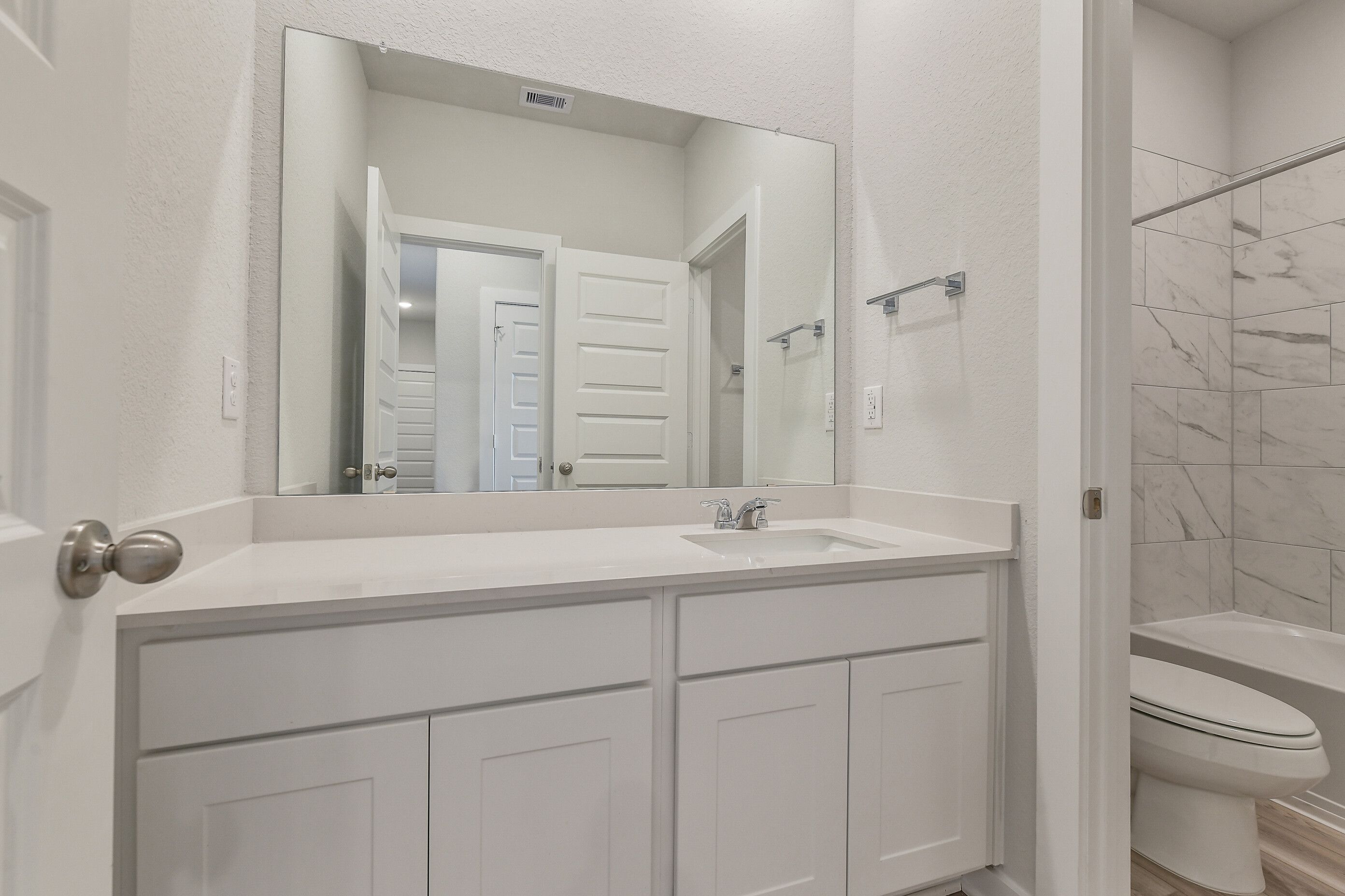 Modern bathroom featuring white shaker vanity, quartz countertop, large frameless mirror, and tiled tub-shower combo in Davidson Homes The Colorado G, Magnolia, Texas