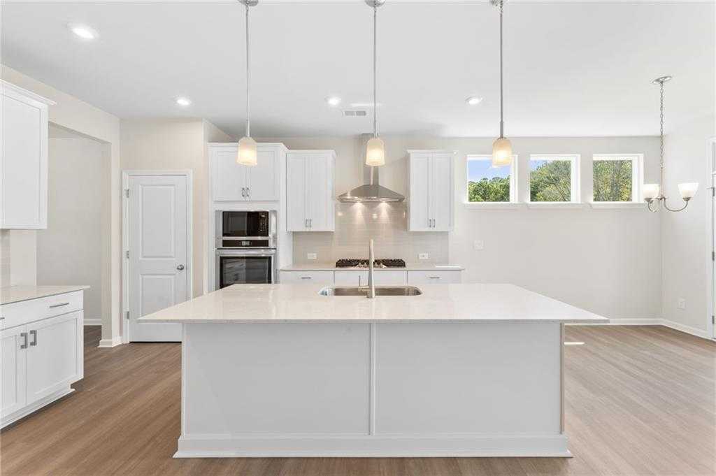 Modern white kitchen with oversized island, stainless appliances, pendant lights in Davidson Homes The Ash B, Riverwood, Dallas, GA