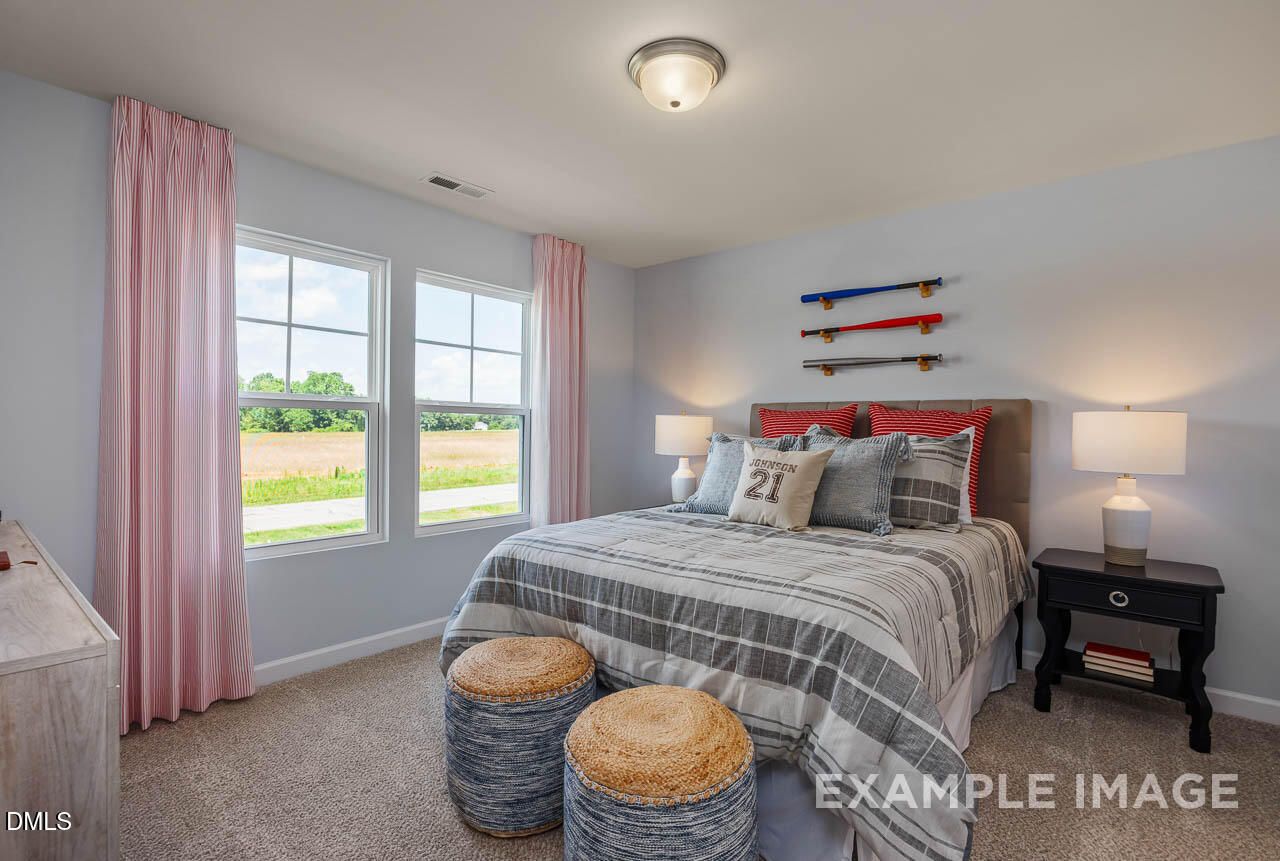 Cozy teen bedroom with gray walls, queen bed, surfboard wall art, and field views through large windows in Davidson Homes The Willow B, Wake Forest, NC