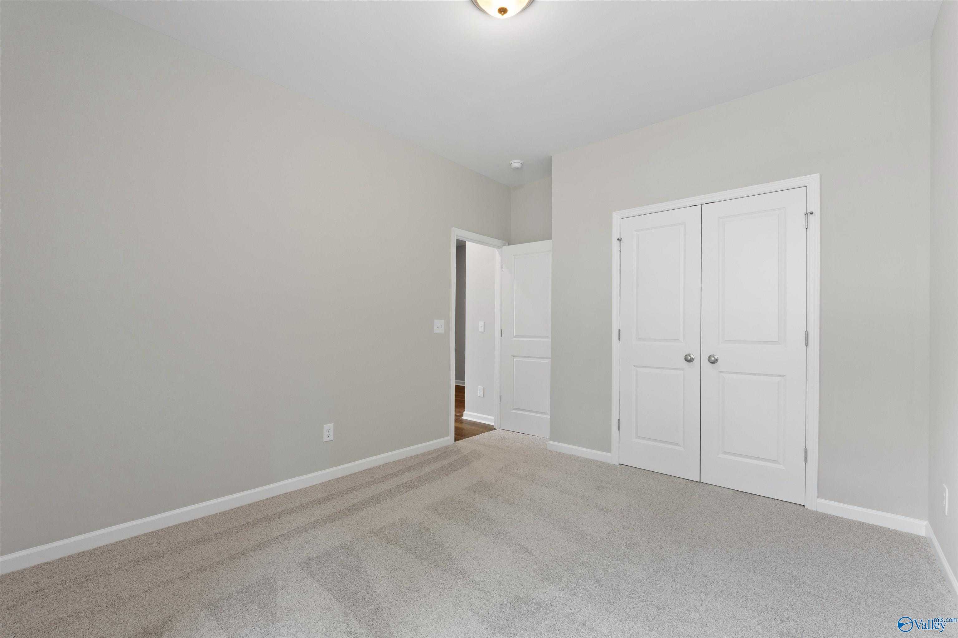 Spacious bedroom with light gray walls, double-door closet, carpet flooring in The Luna floor plan by Davidson Homes, Hazel Green, Alabama