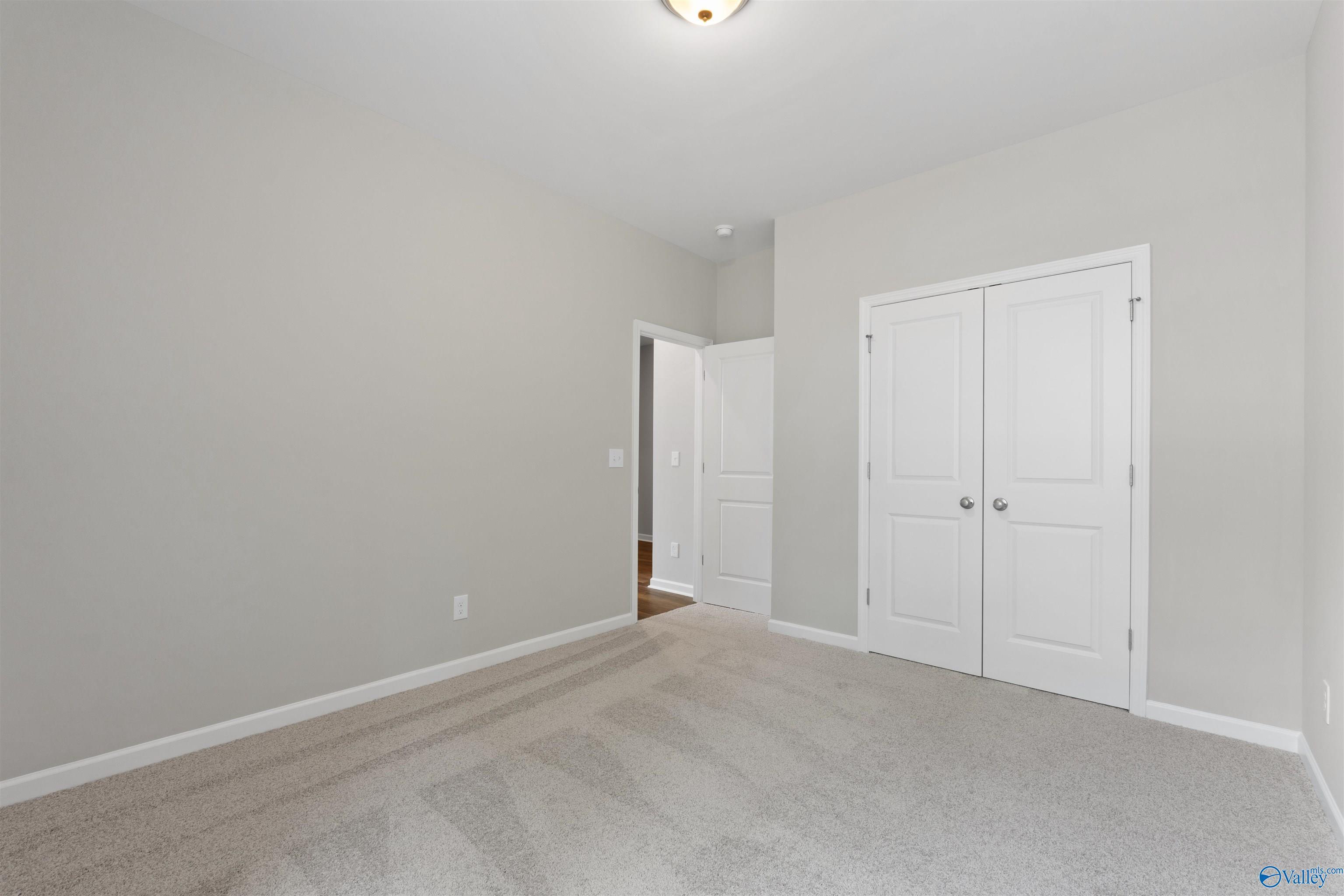 Spacious bedroom with light gray walls, double-door closet, carpet flooring in The Luna floor plan by Davidson Homes, Hazel Green, Alabama