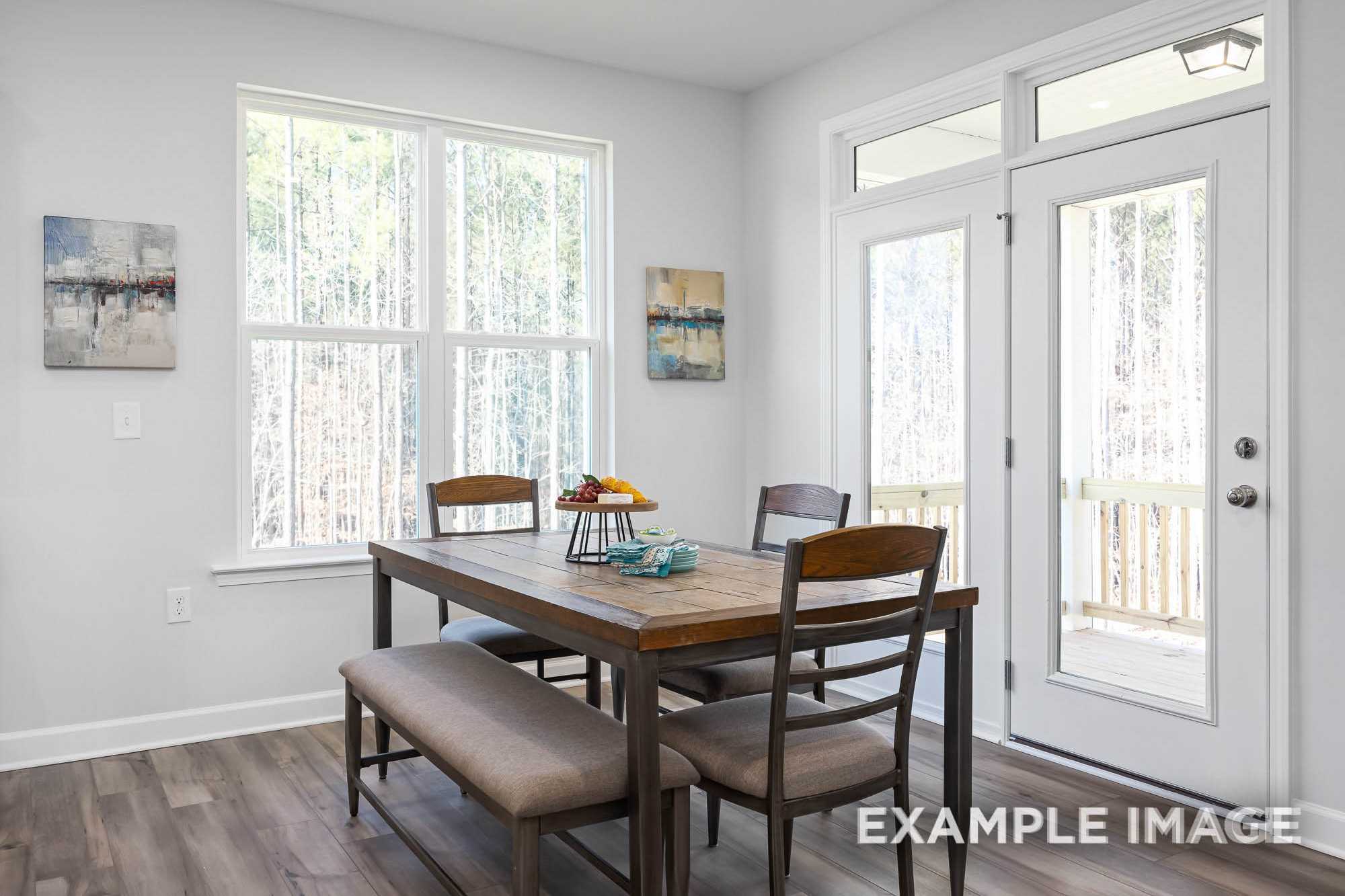 Spacious The Ash B dining room with wooden farmhouse table, bench seating, fruit centerpiece, large windows, and French doors to deck