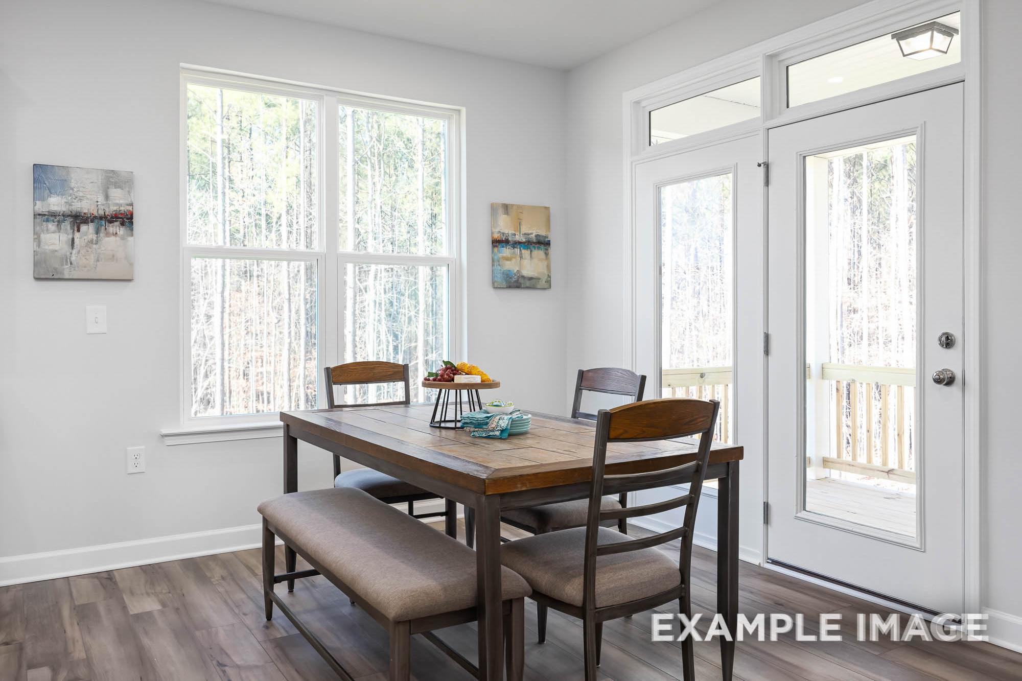 Spacious dining room in The Ash home with wooden table, bench seating, fruit centerpiece, and French doors to deck