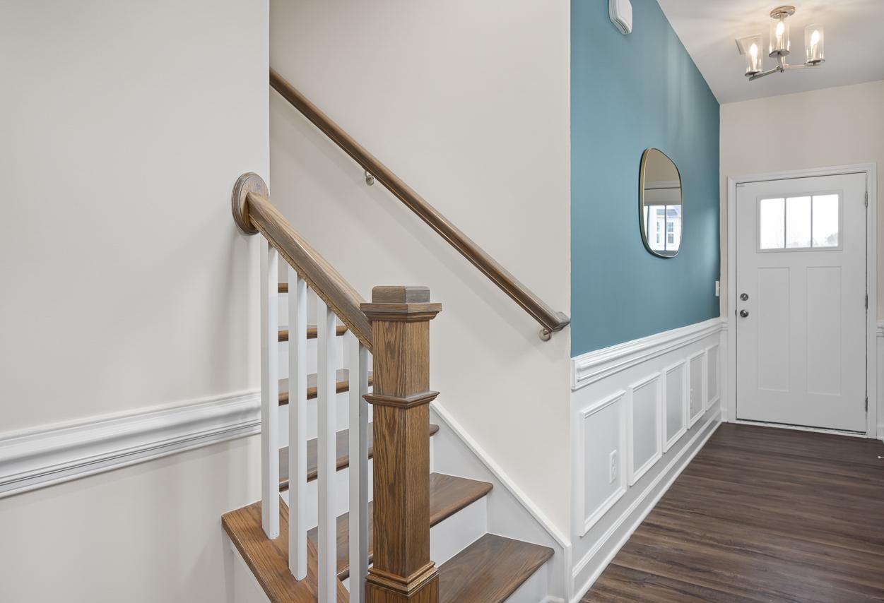 Foyer and staircase in The Wake home design featuring wainscoting, a teal accent wall, and wood-tread stairs.