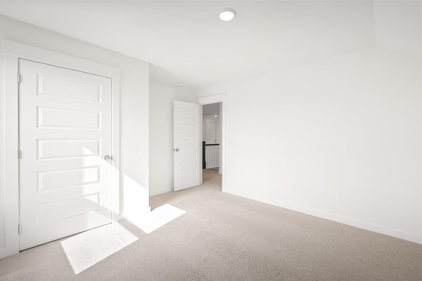 Bright secondary bedroom with white paneled door, open bath access, and beige carpet in Davidson Homes The Ash C, Mt. Juliet