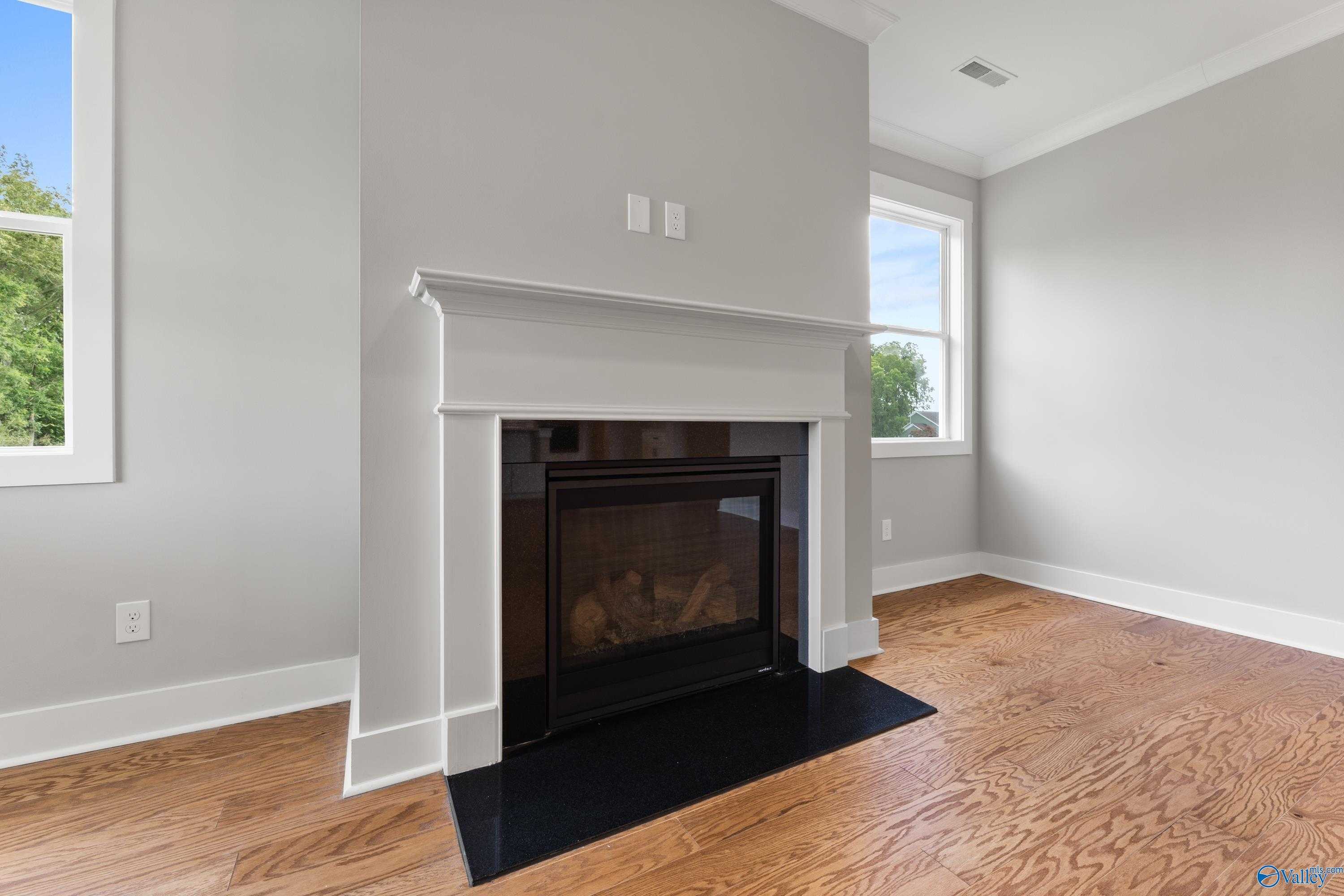 Cozy gas fireplace with white mantel in gray-walled living room, hardwood floors, large windows in Davidson Homes The Arcadia, Huntsville AL