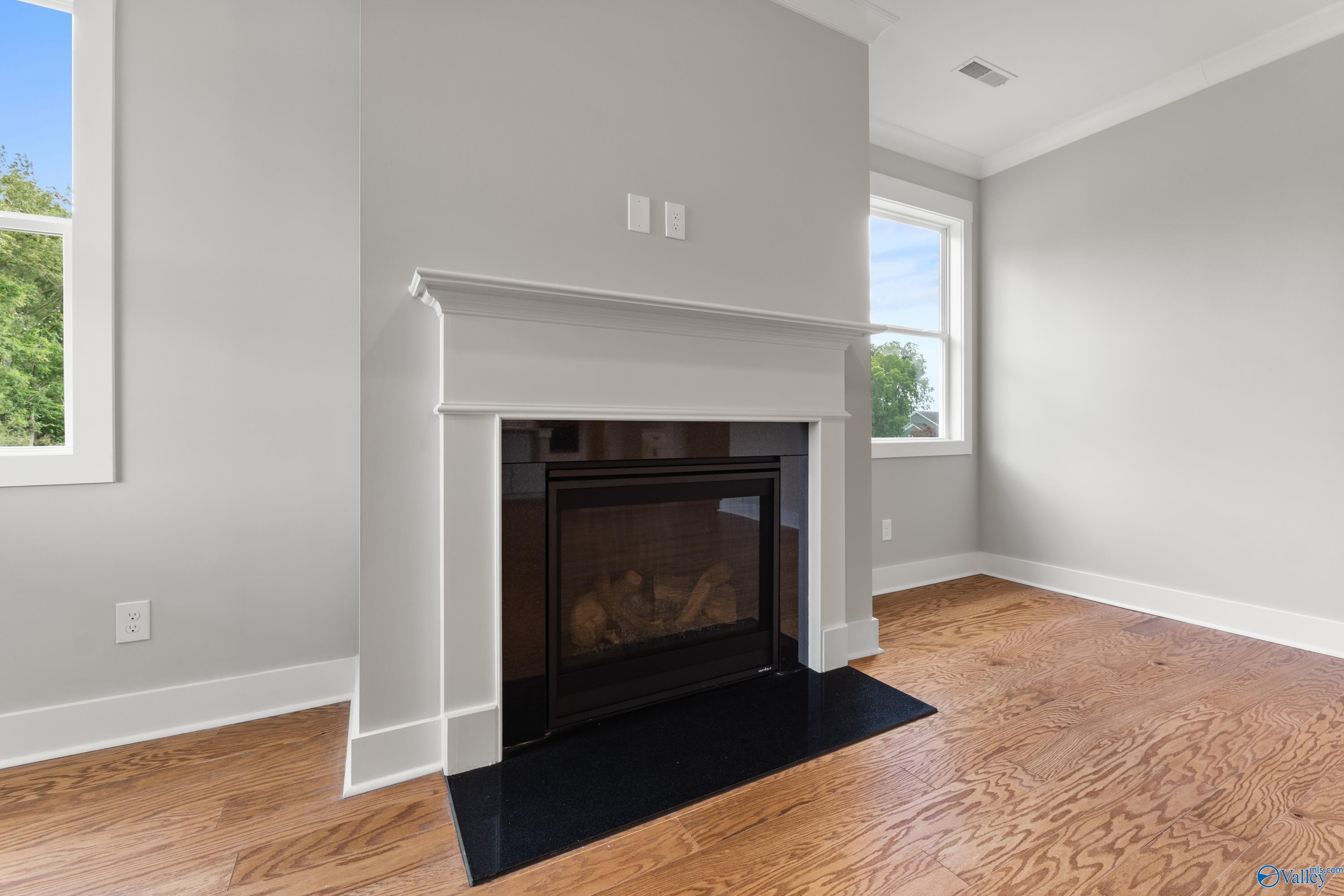 Cozy gas fireplace with white mantel in gray-walled living room, hardwood floors, large windows in Davidson Homes The Arcadia, Huntsville AL