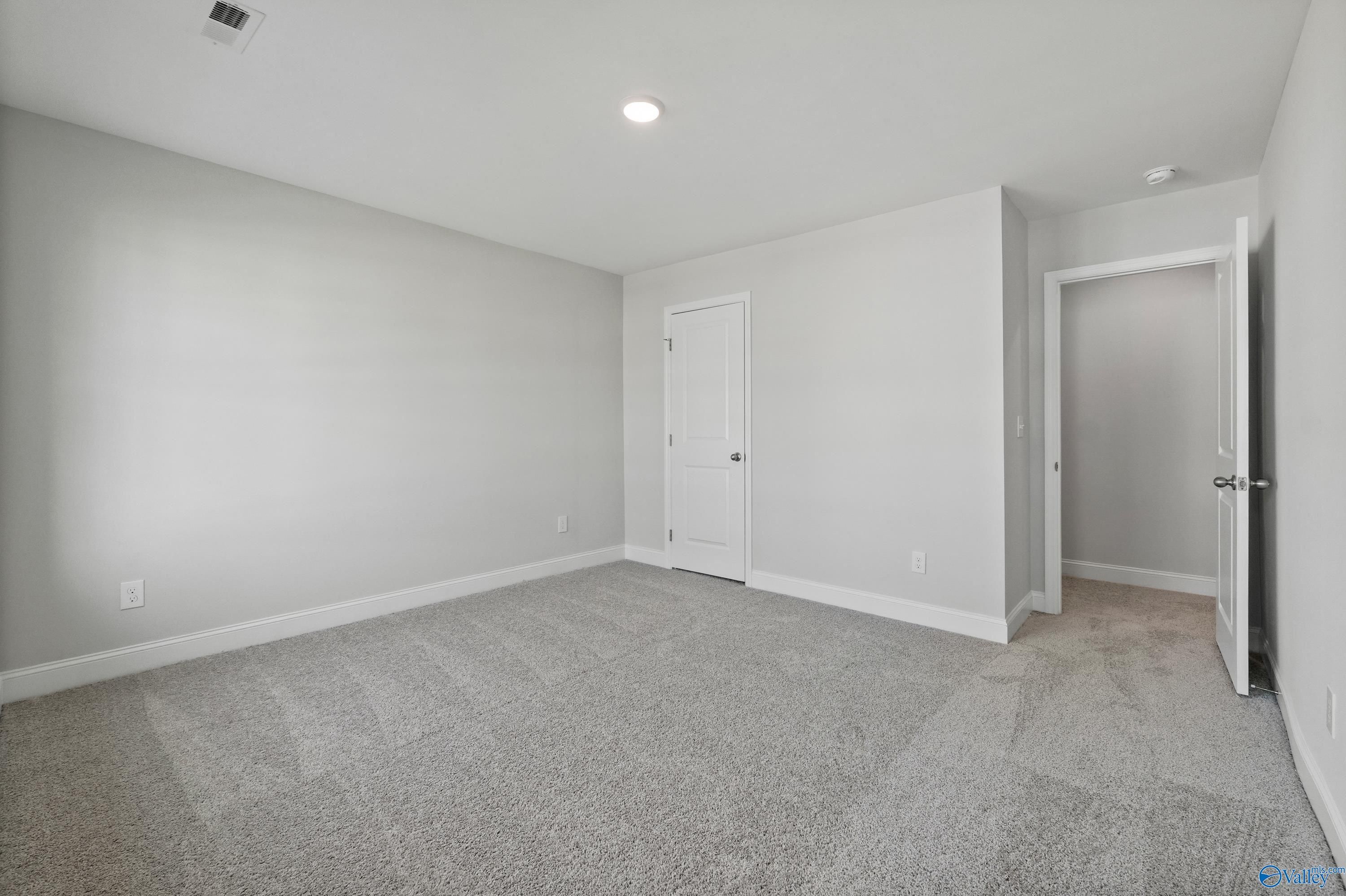 Spacious empty bedroom with gray carpet, light gray walls, and double doors in Davidson Homes The Camden, Huntsville, Alabama