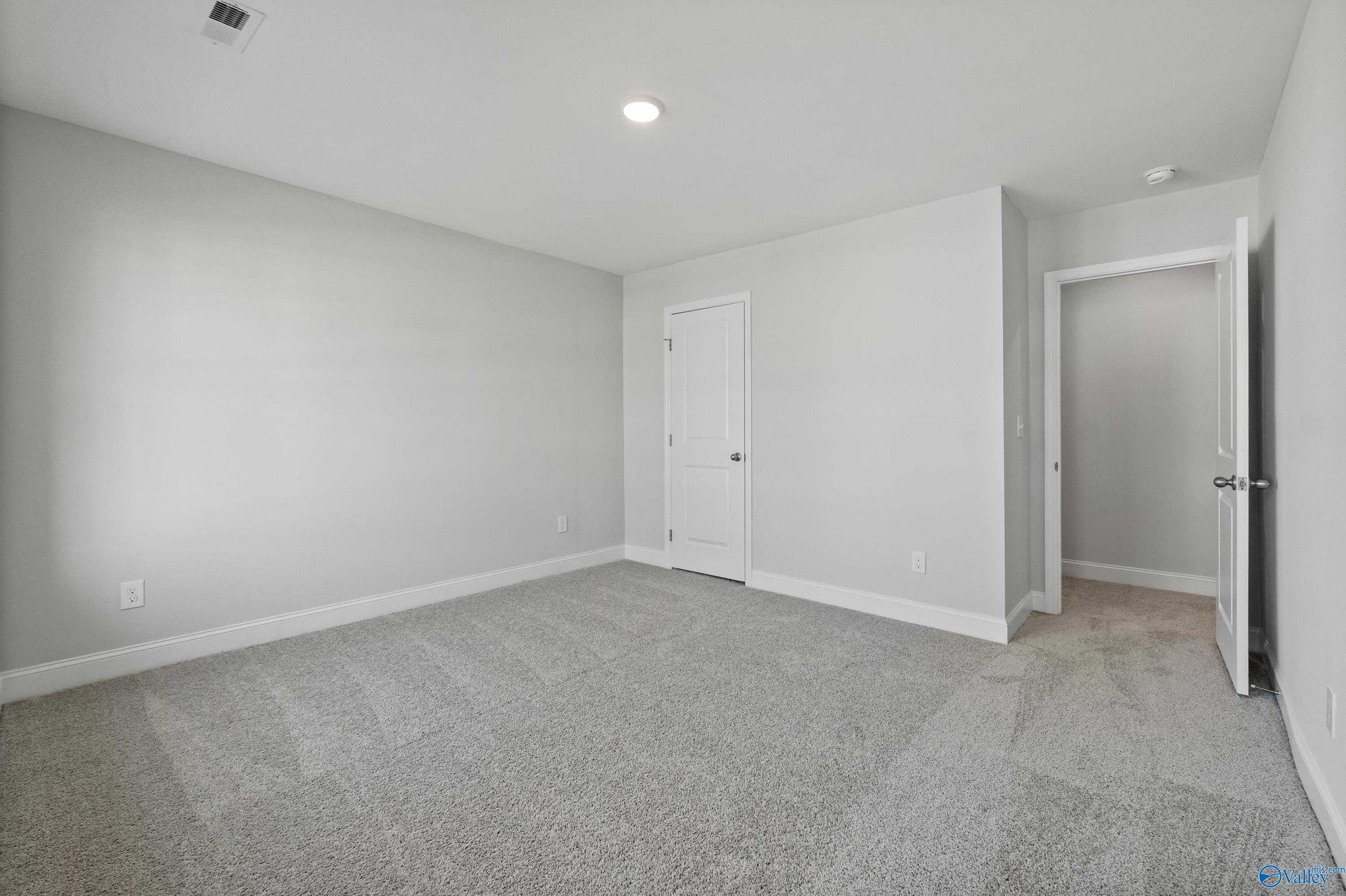 Spacious empty bedroom with gray carpet, light gray walls, and double doors in Davidson Homes The Camden, Huntsville, Alabama