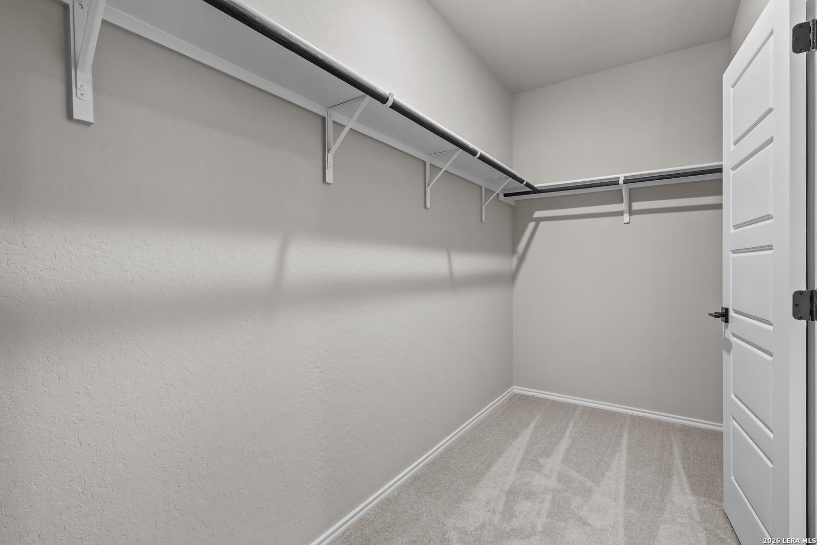 Walk-in closet with shelving and carpeted floors in The Daphne H floor plan, Hannah Heights, Seguin home.