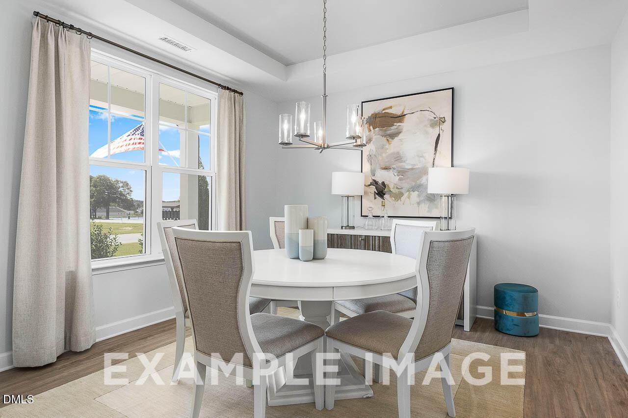 Bright formal dining room with round white table, upholstered chairs, and modern chandelier in Davidson Homes The Ash C, Lillington NC