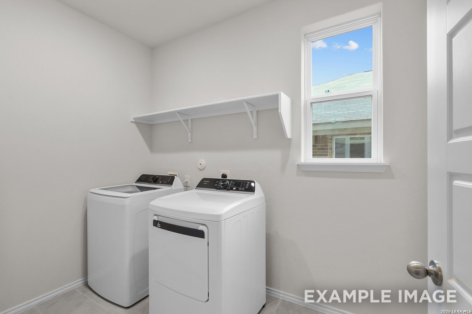 Laundry room with white washer and dryer, wall shelving, and window in The Sequoia C home at Royal Crest, San Antonio.
