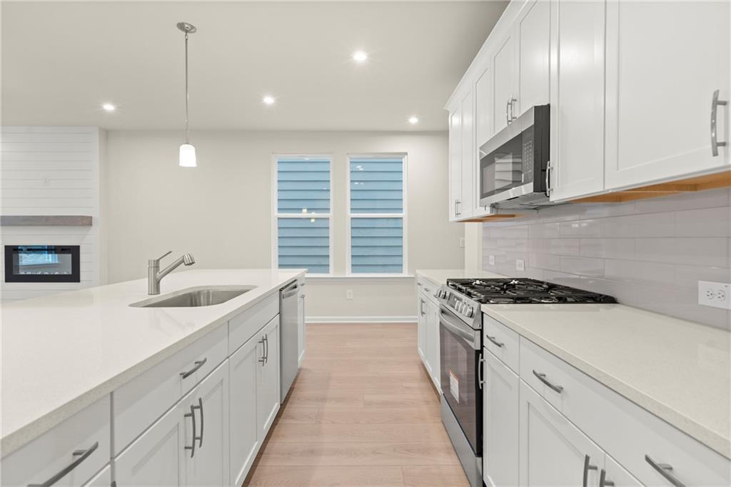Bright open-concept kitchen with white shaker cabinets, quartz island, stainless appliances, and fireplace in Davidson Homes The Cary A, Kennesaw, GA