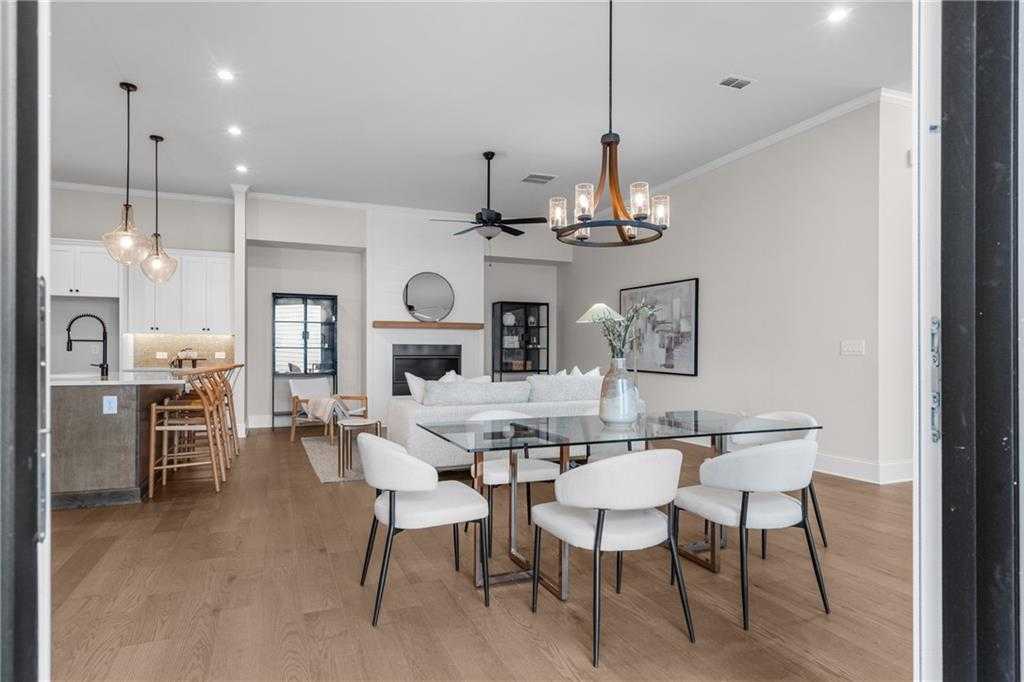 Open-concept living and dining area with glass table, white chairs, fireplace, round mirror, and kitchen in The Seaside B home, Woodstock, Georgia
