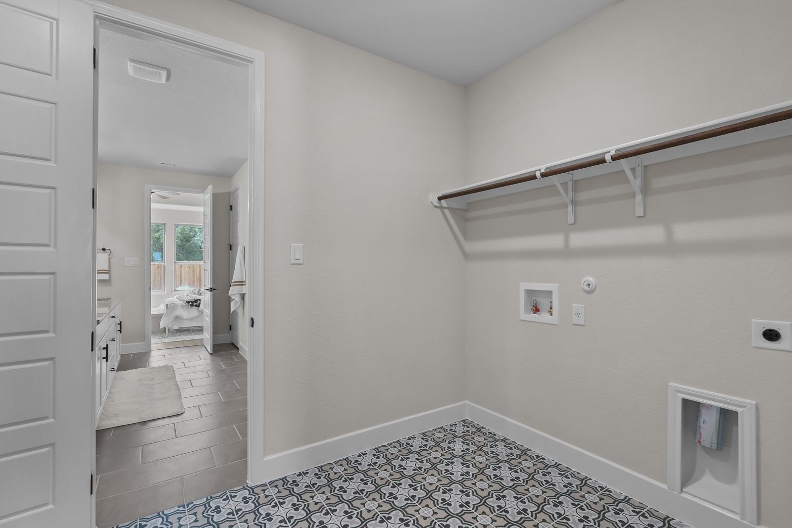 Spacious laundry room in The Belmont with stylish patterned tile flooring, shelving, and easy access to the master bath.