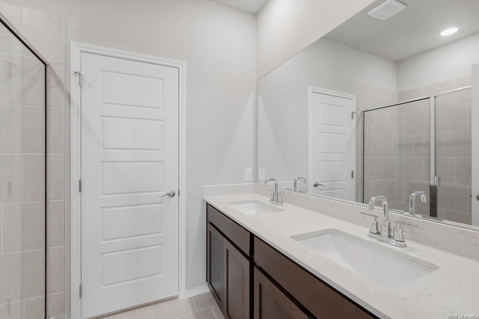 Modern master bathroom with double quartz vanity, dark wood cabinets, frameless glass shower in Davidson Homes The Frio B, San Antonio