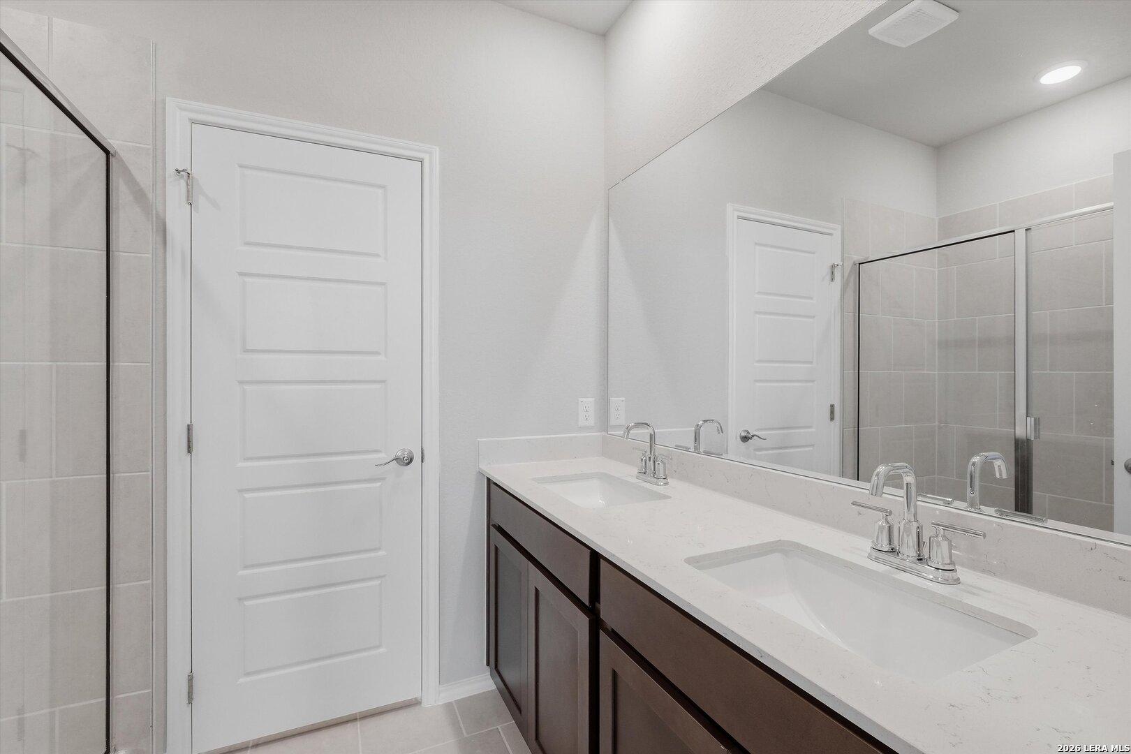 Modern master bathroom with double quartz vanity, dark wood cabinets, frameless glass shower in Davidson Homes The Frio B, San Antonio