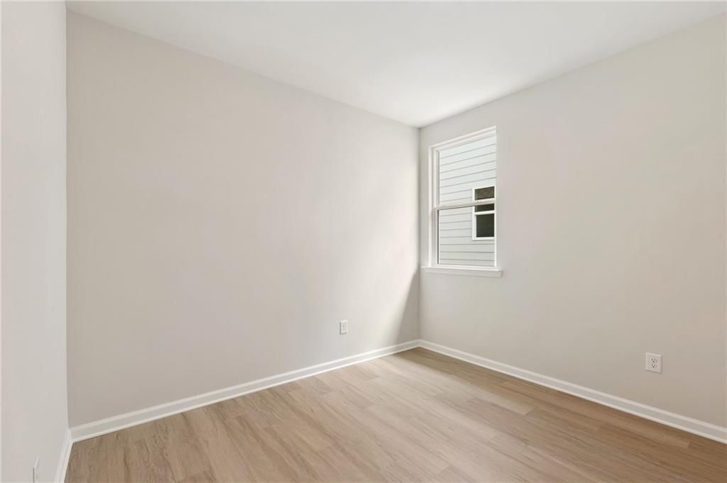 Bright empty bedroom with neutral walls, large window, and light oak hardwood floors in The Daphne C, Kelly Preserve, Loganville, GA