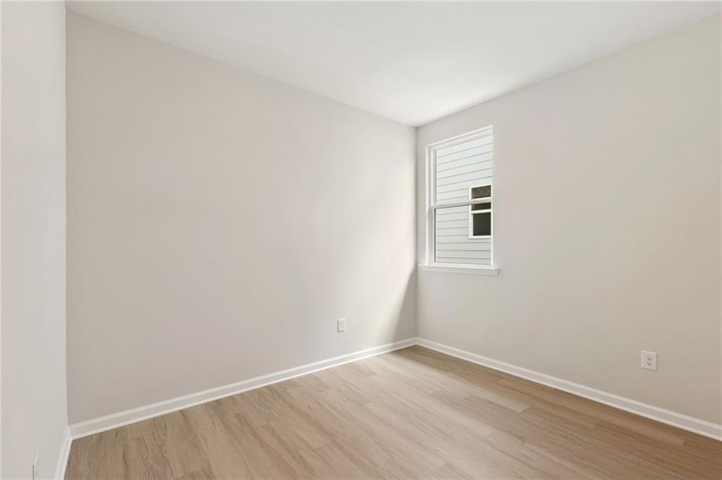 Bright empty bedroom with neutral walls, large window, and light oak hardwood floors in The Daphne C, Kelly Preserve, Loganville, GA