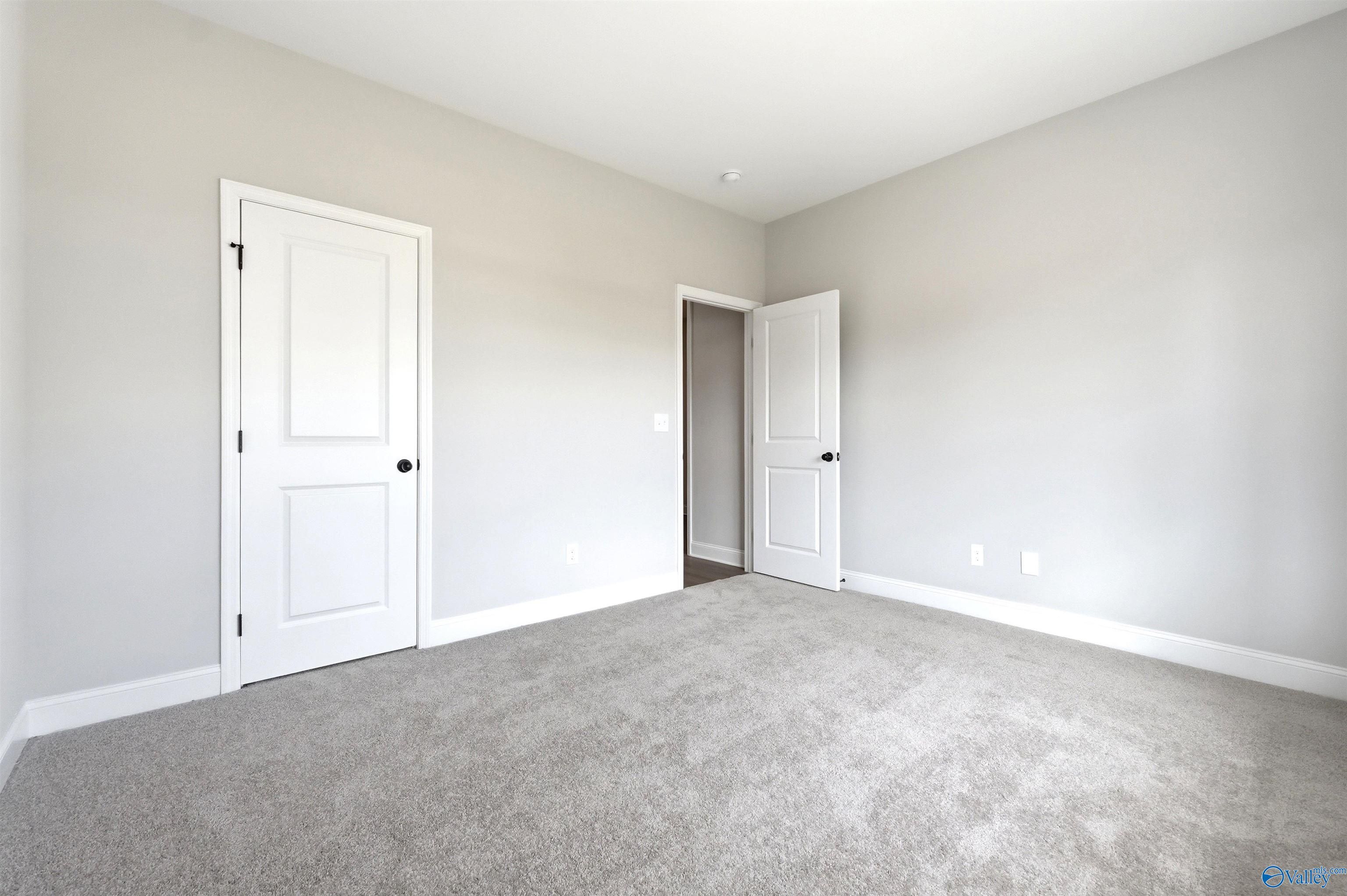 Spacious secondary bedroom with neutral carpet and white doors in The Daphne F floor plan at Berry Cove, New Market, AL.