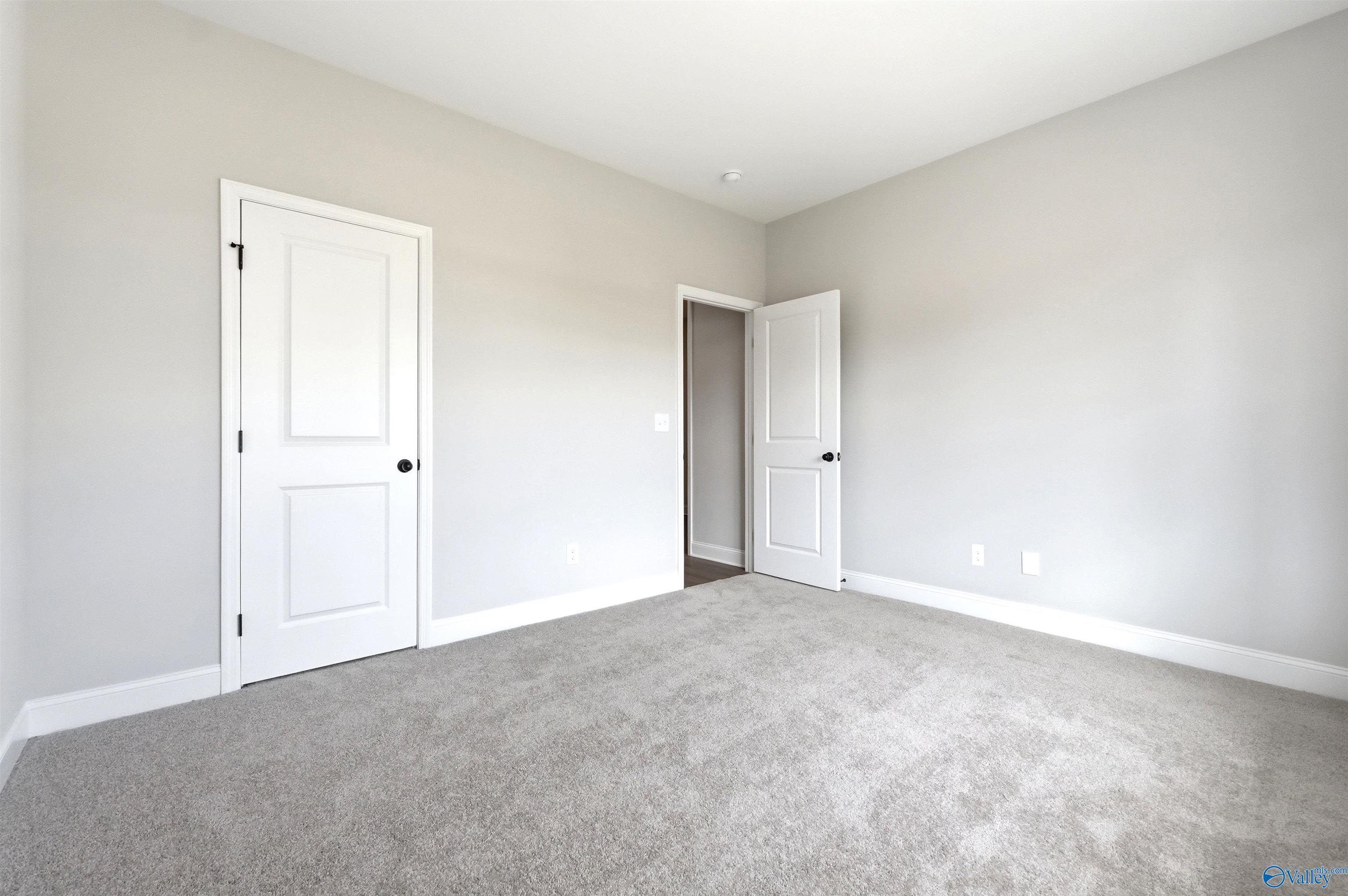 Spacious secondary bedroom with neutral carpet and white doors in The Daphne F floor plan at Berry Cove, New Market, AL.