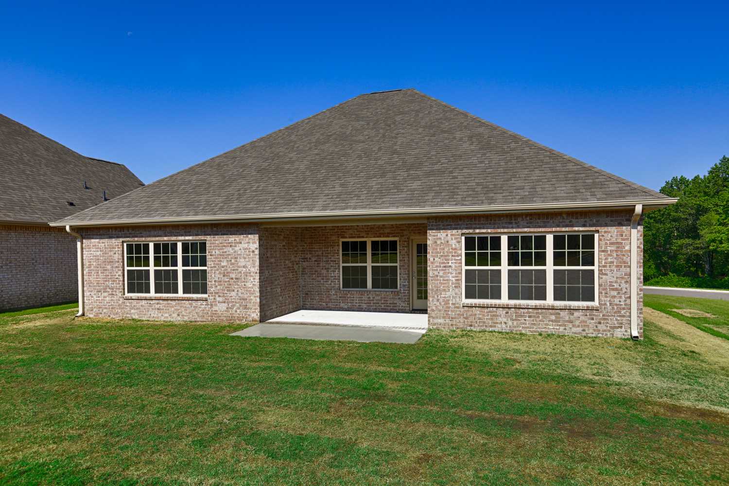 Rear elevation of The Montgomery single-story brick home with gabled roof, large windows, covered porch, and lush lawn in Meridianville, AL