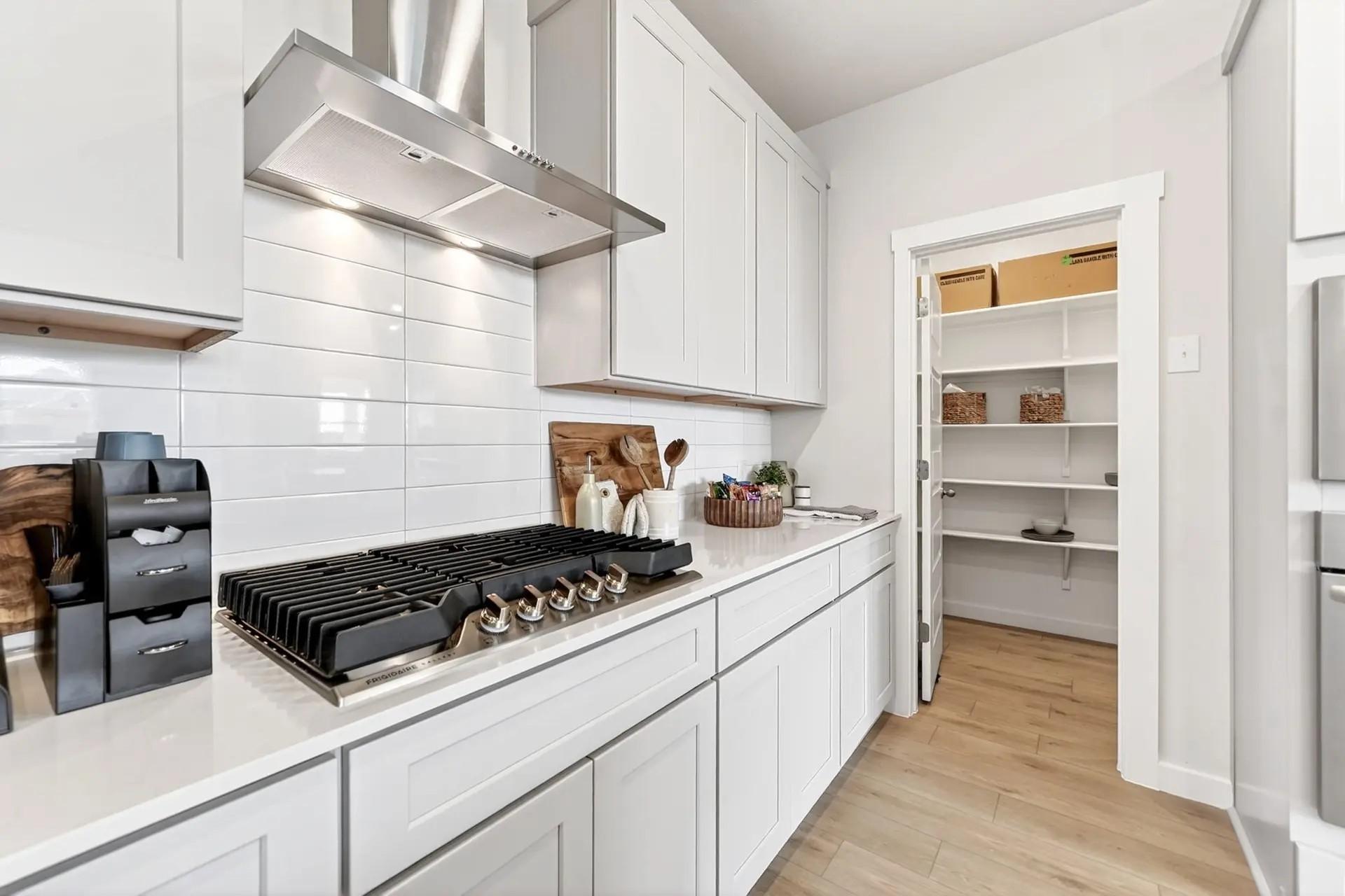 Modern kitchen with white cabinets, gas range, and walk-in pantry in The Laurel I floor plan by Davidson Homes in Heartland.