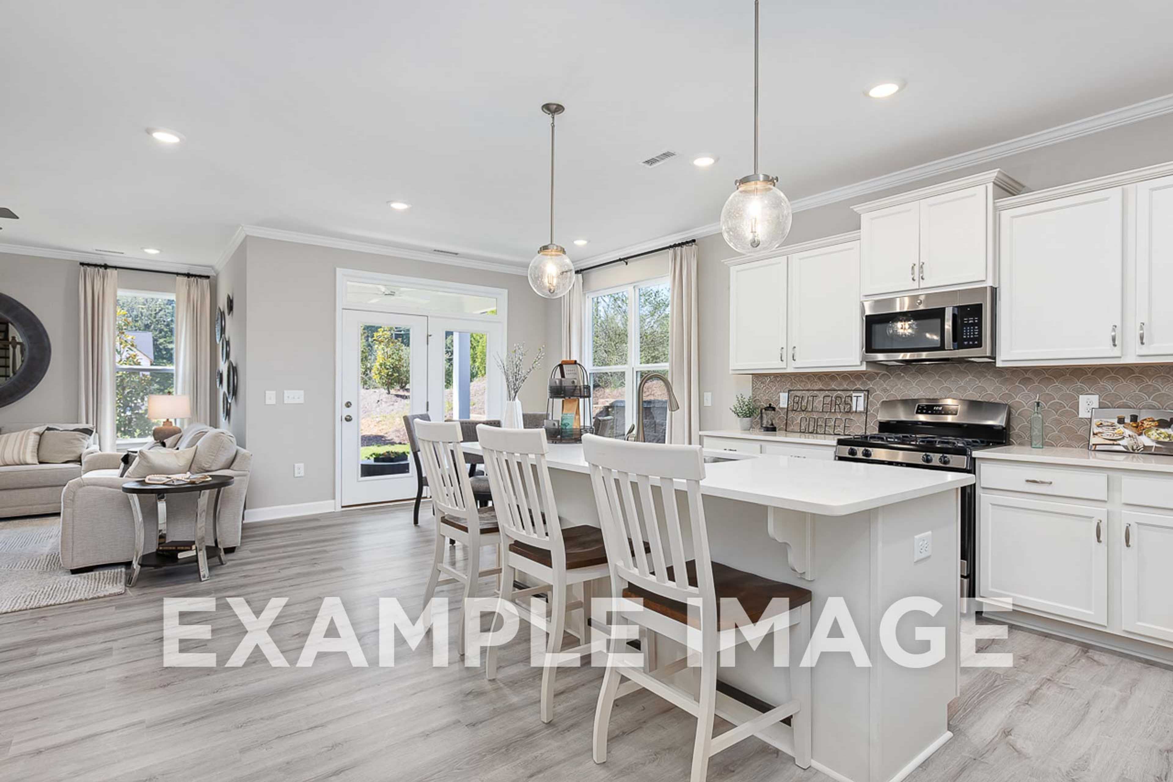 Spacious open-concept kitchen in The Ash home design featuring white cabinets, large island, dining table, and living area