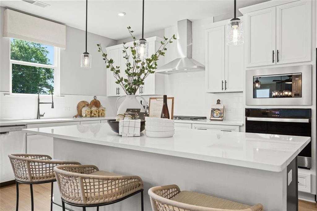 Modern white kitchen with quartz island, stainless appliances, rattan bar stools in Davidson Homes The Hickory B, Hoschton, GA