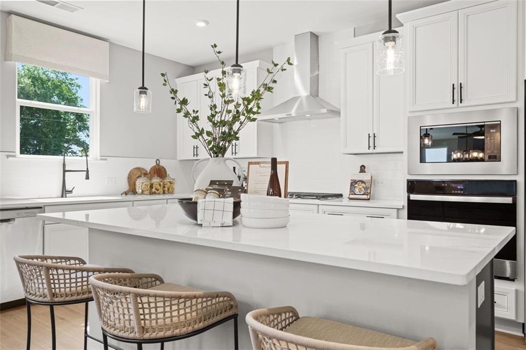 Modern white kitchen with quartz island, stainless appliances, rattan bar stools in Davidson Homes The Hickory B, Hoschton, GA