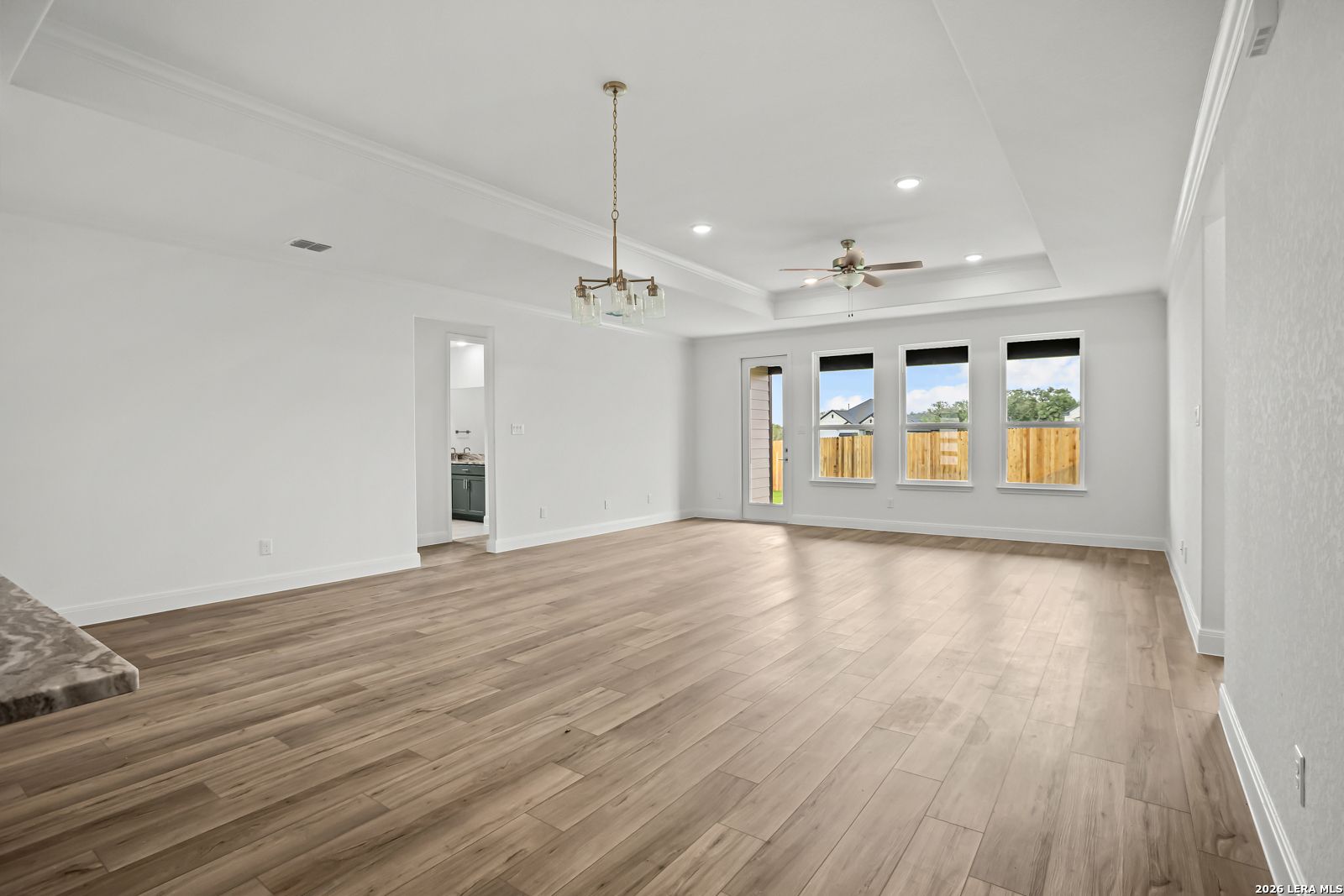 Spacious open-concept living room with tray ceiling and wood-look floors in The Lanier G floor plan, Castroville, Texas.