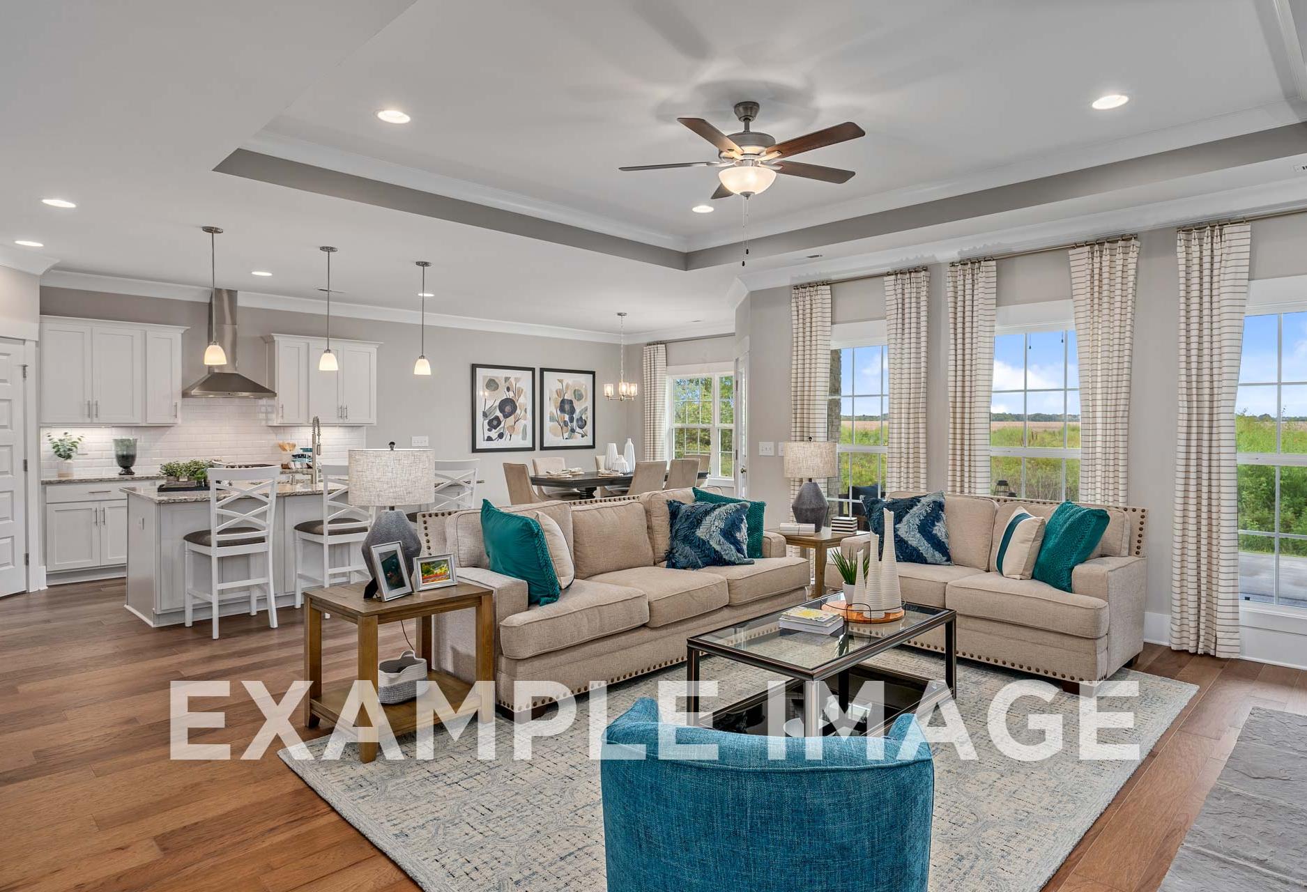 Spacious open-concept living room in The Harrison Davidson Homes design with L-shaped sofa, teal accents, kitchen island, and scenic windows