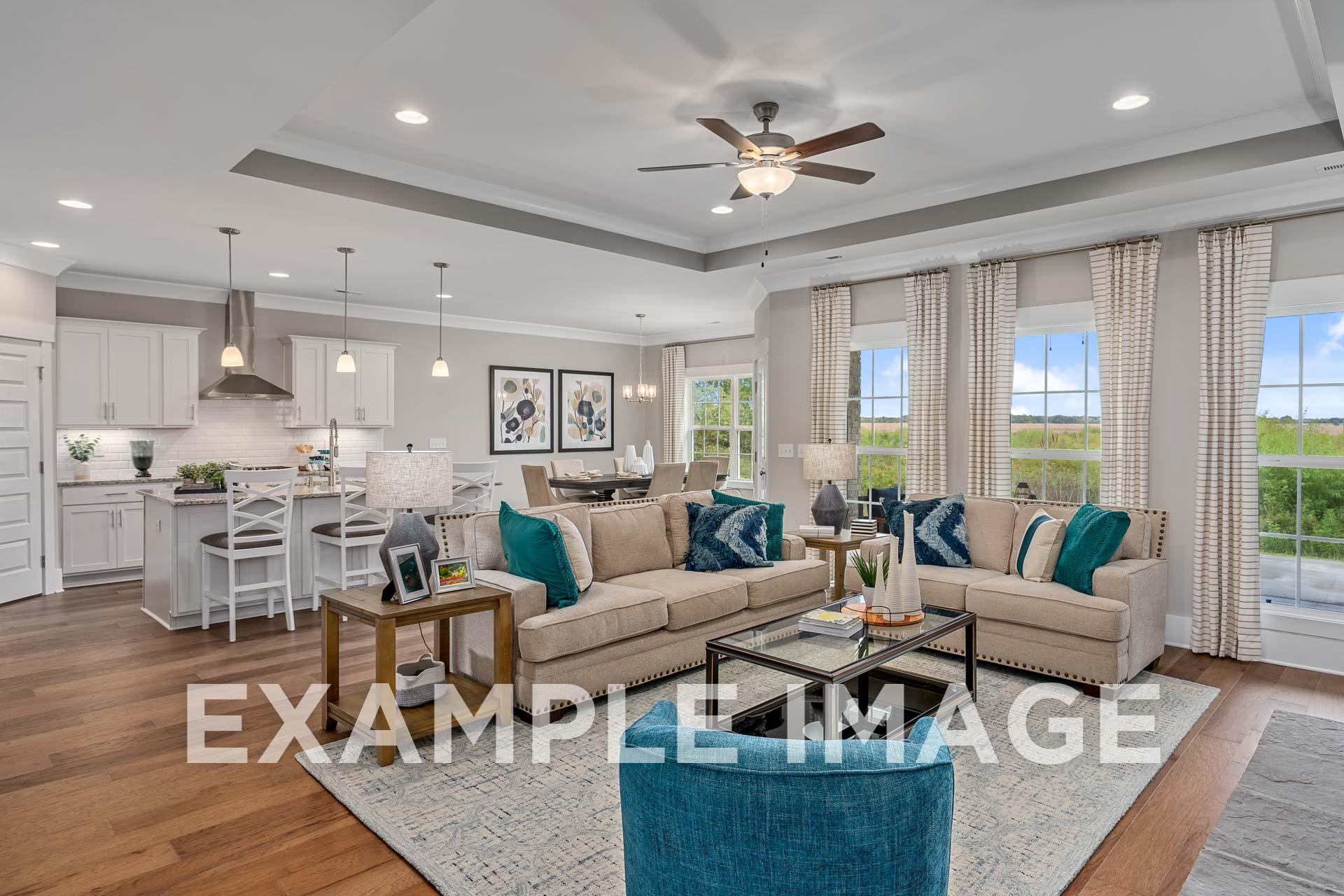 Spacious open-concept living room in The Harrison B home design with beige L-shaped sofa, blue accents, hardwood floors, and adjacent white kitchen island