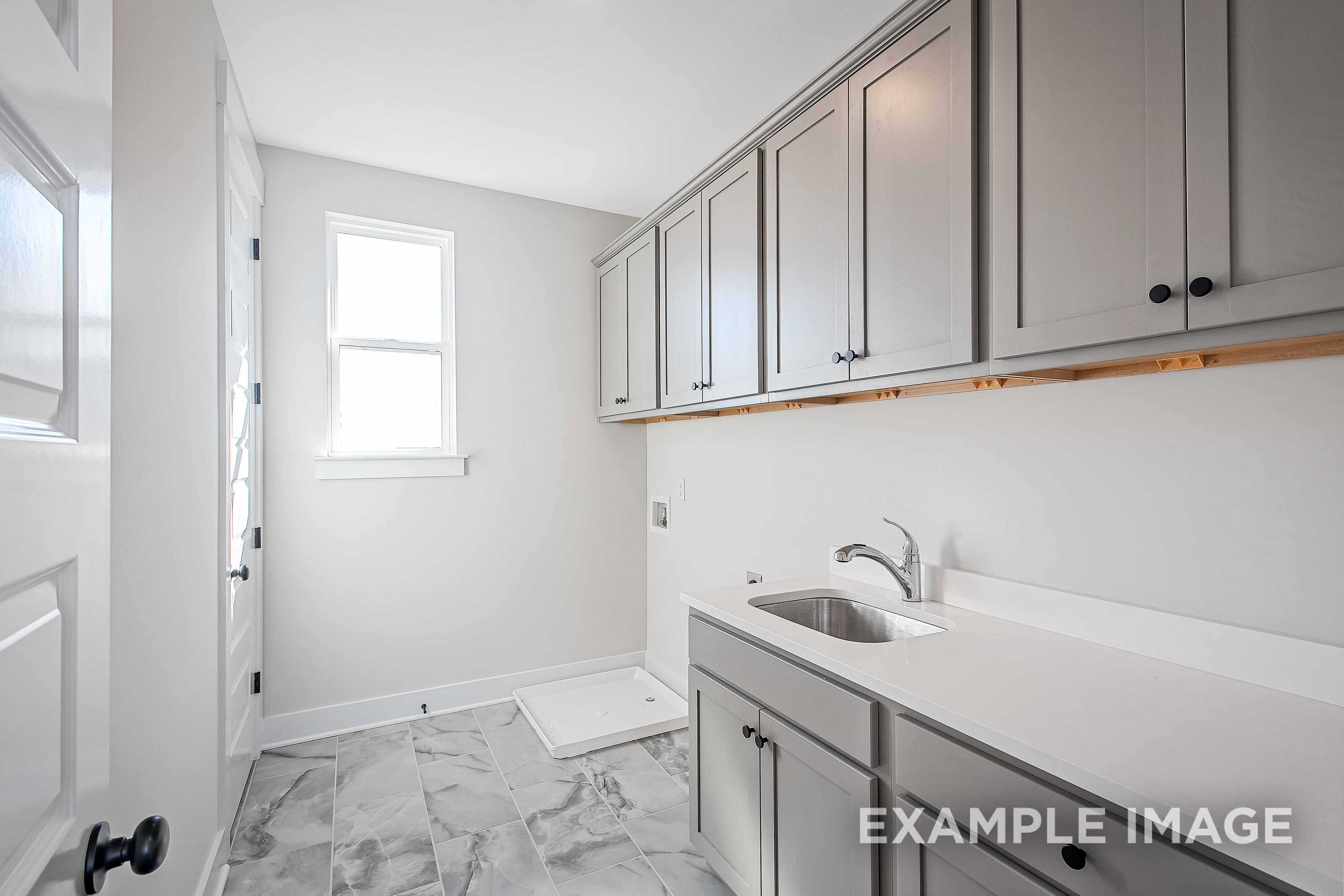 Modern laundry room in The Alston A showcasing gray shaker cabinets, utility sink, and tiled flooring